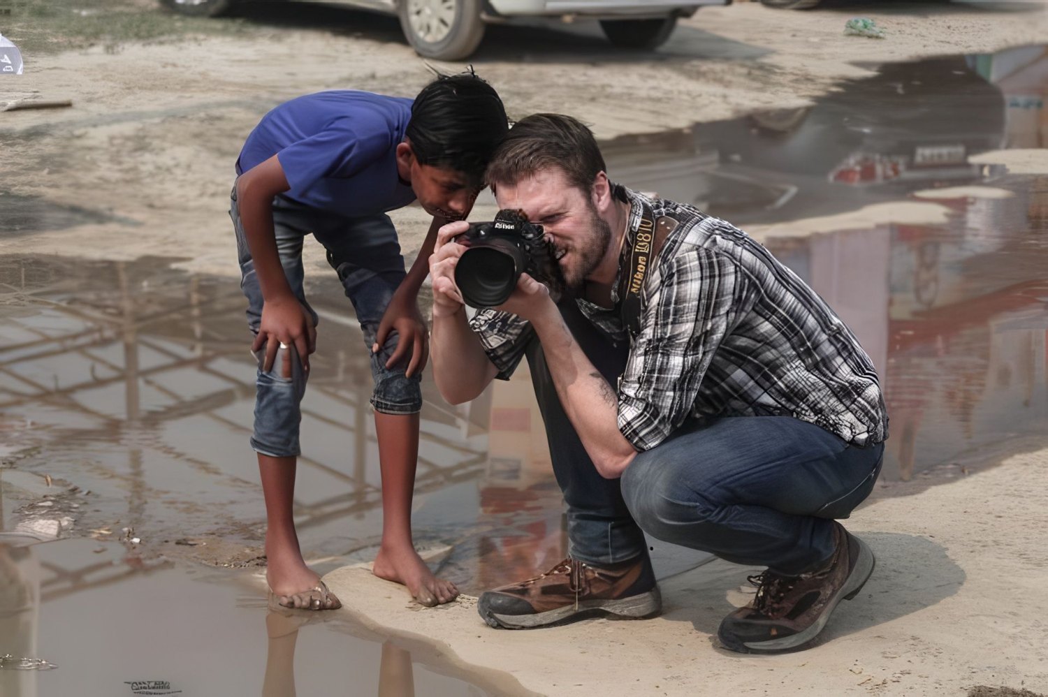 Tyler crouched with his camera beside a boy looking at the screen, at the Kumbh Mela