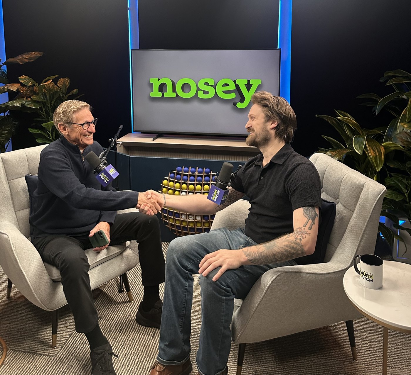 Tyler Blodgett shaking hands with Maury Povich in a studio, the Nosey logo on the screen behind them