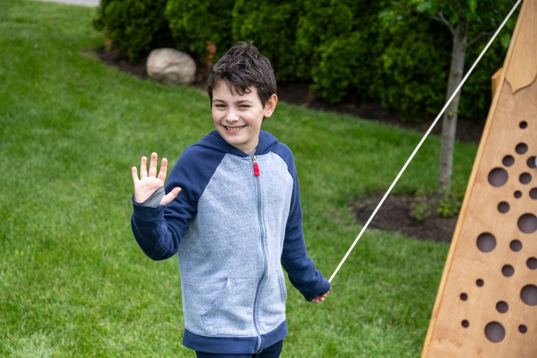A boy waves on his way past the wooden hole board.