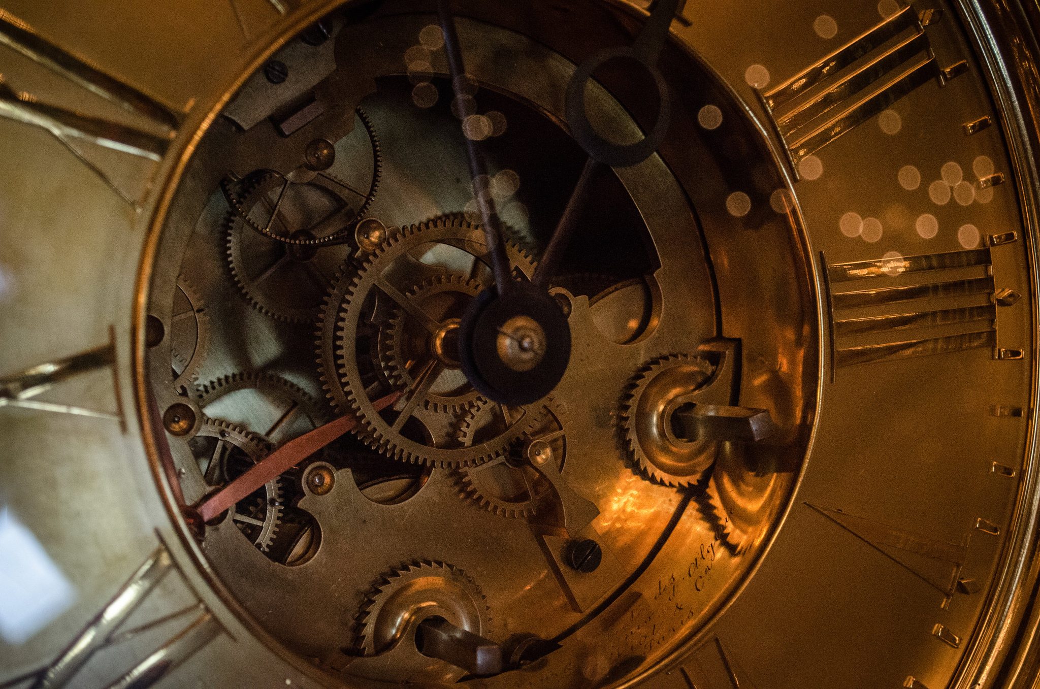 Brass gears turn behind the glass of an old clock.