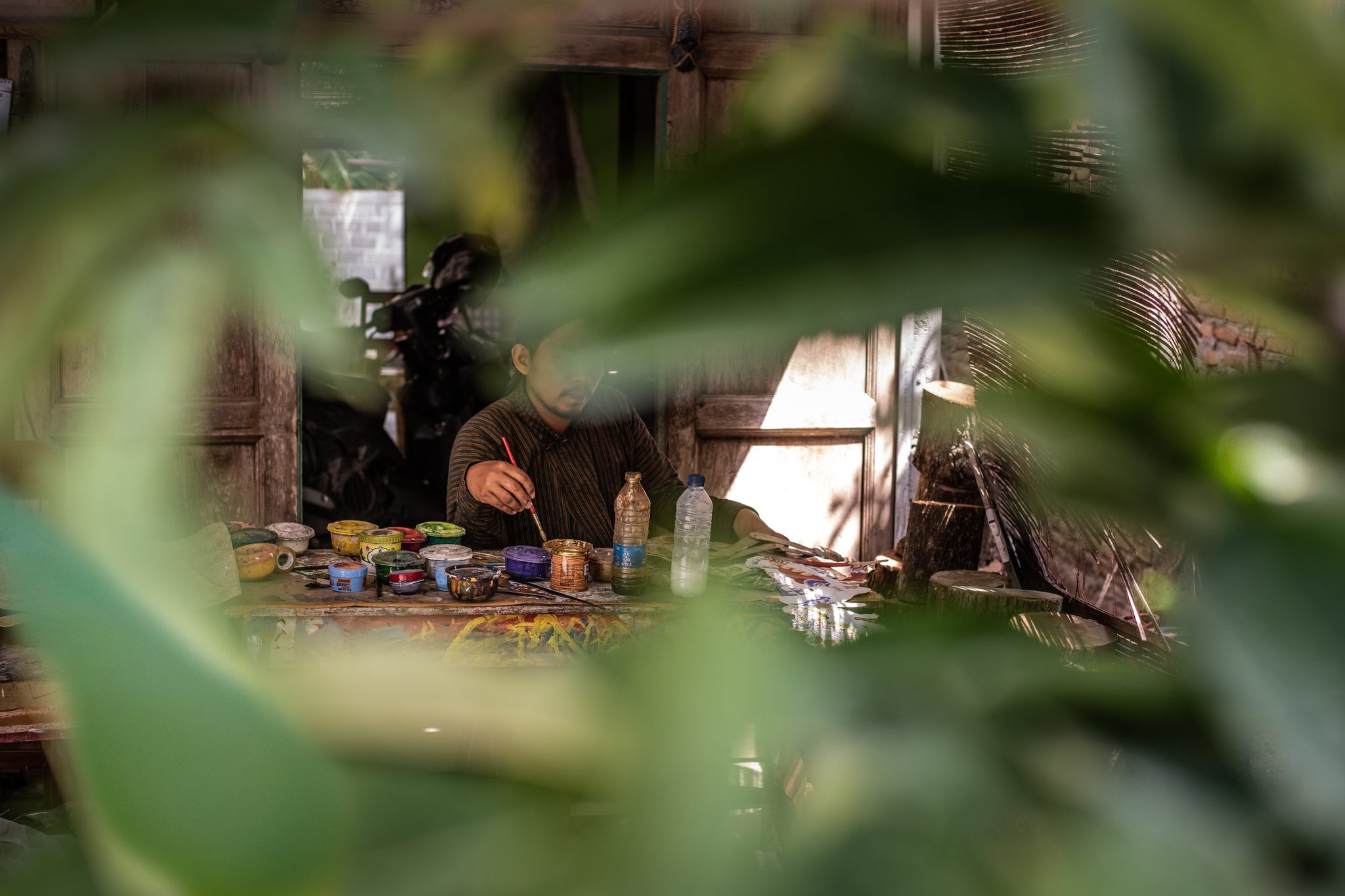 Through the leaves, the painter bends over his table of colors.