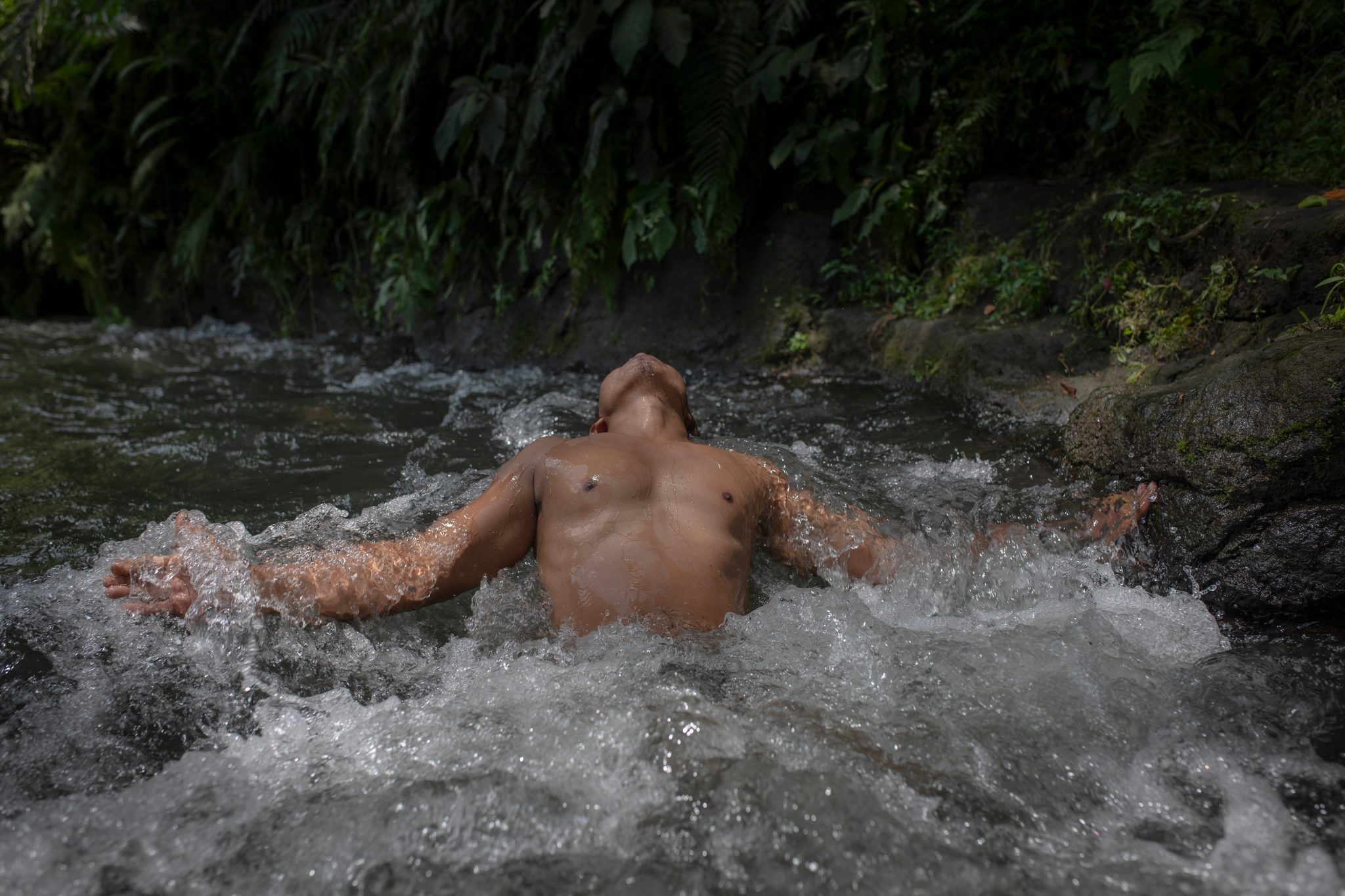 A man throws his arms wide as the river rushes over him.