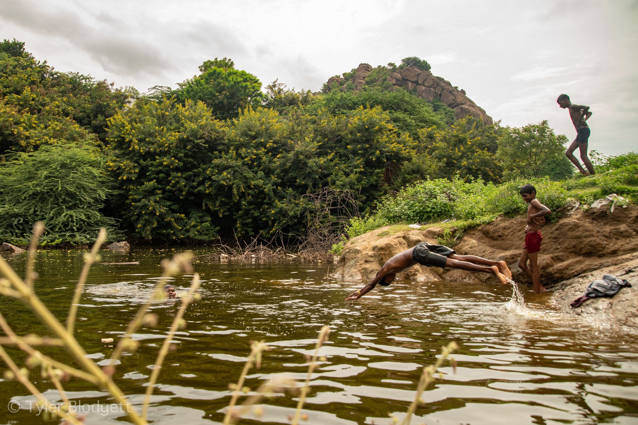 One boy hits the water as another climbs the rock for his turn.