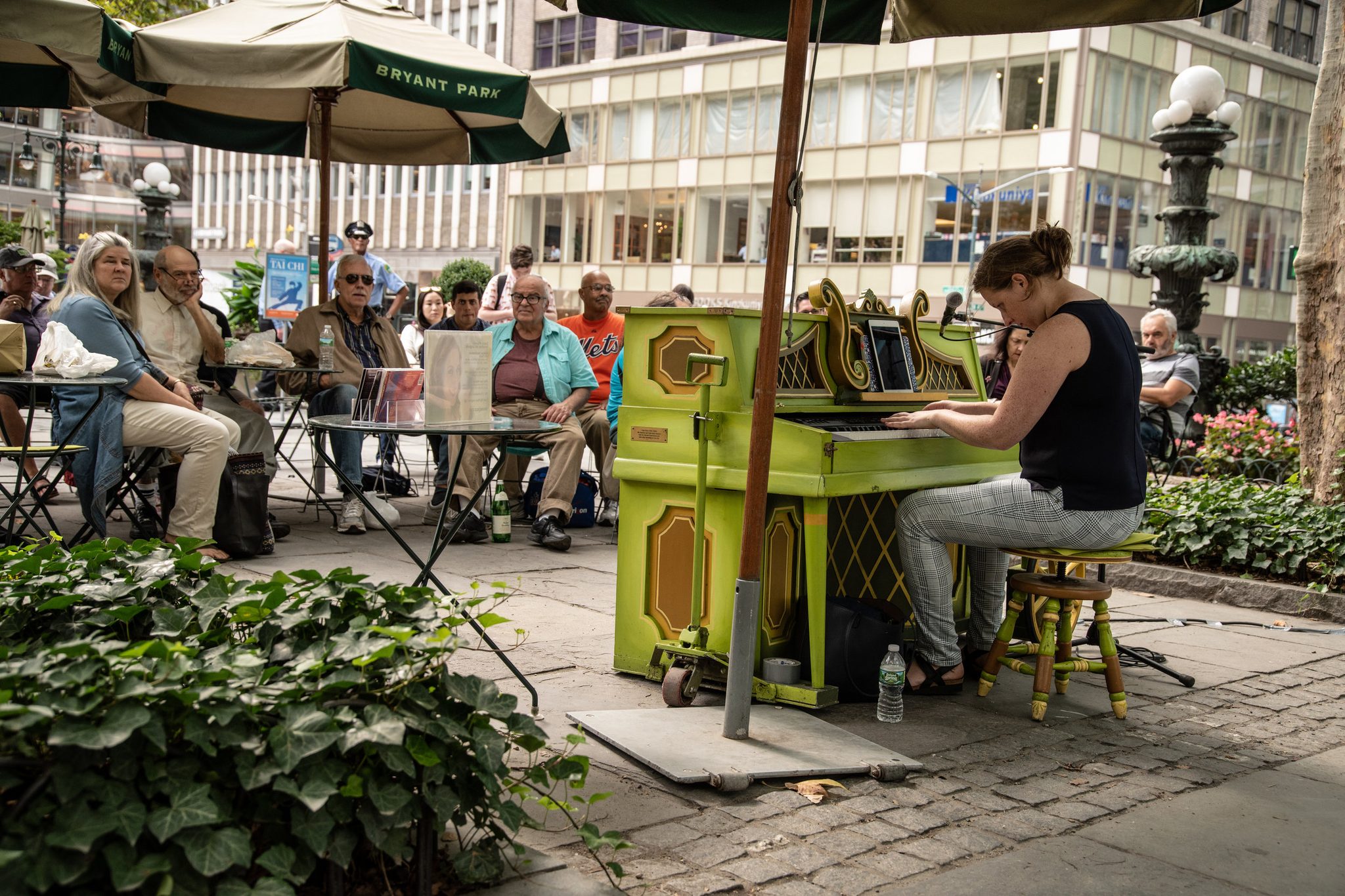 A woman plays the green piano in Bryant Park while the lunch crowd listens from the tables.