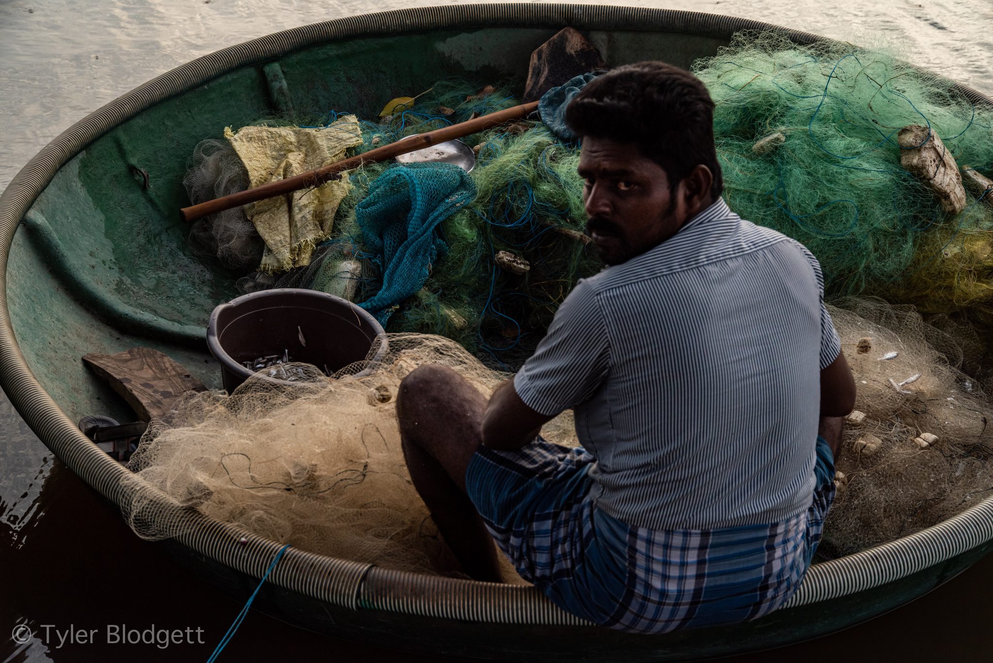 He glances up from the net, the coracle heaped with green mesh.
