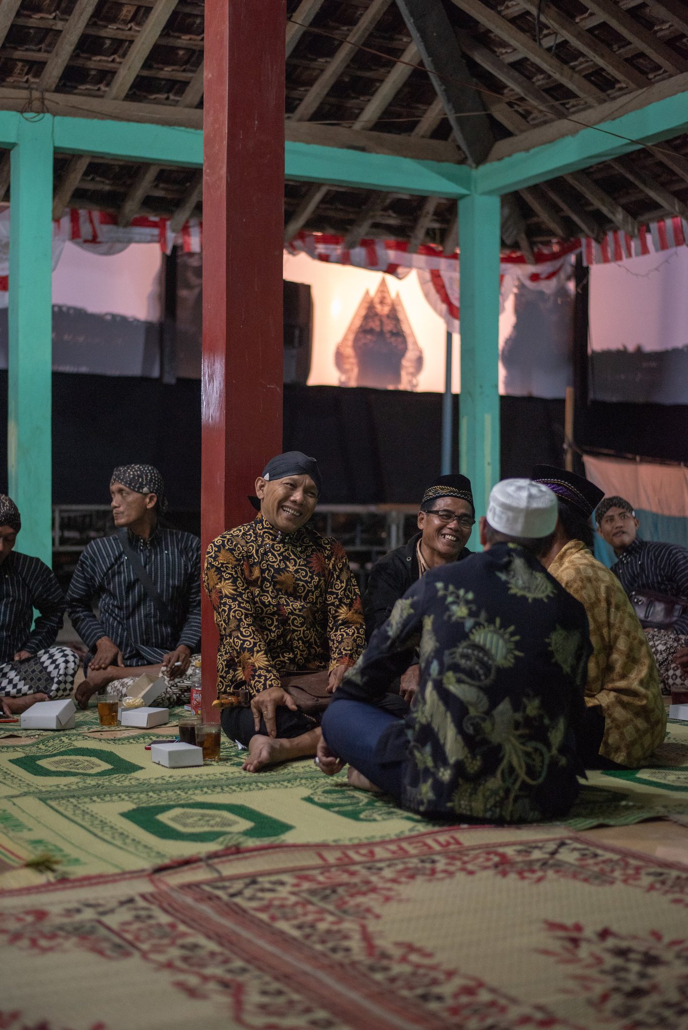 Men in batik settle onto the mats in the pavilion. The screen and its puppets are already waiting.