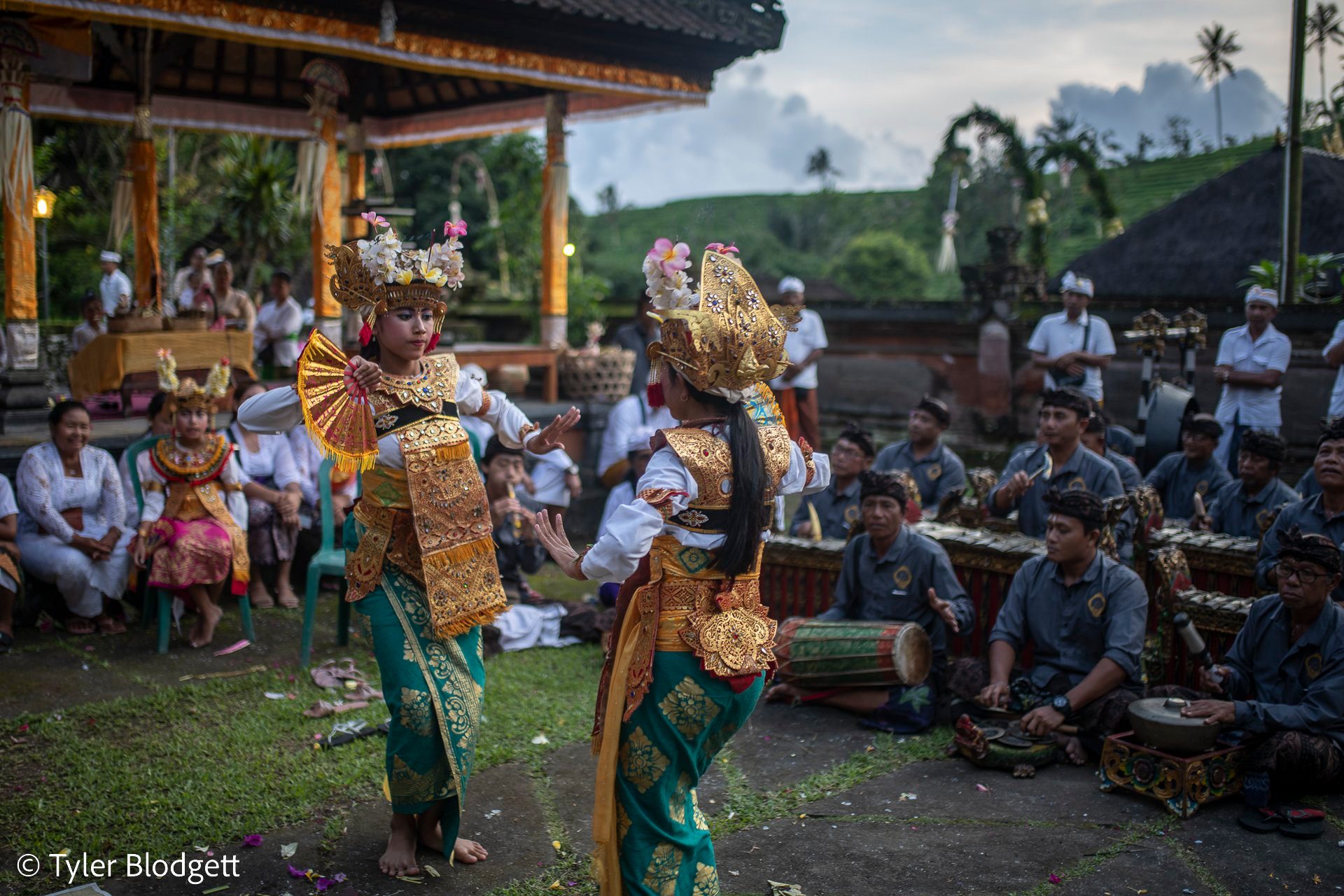 Two young dancers in gold move to the gamelan while the temple courtyard looks on.