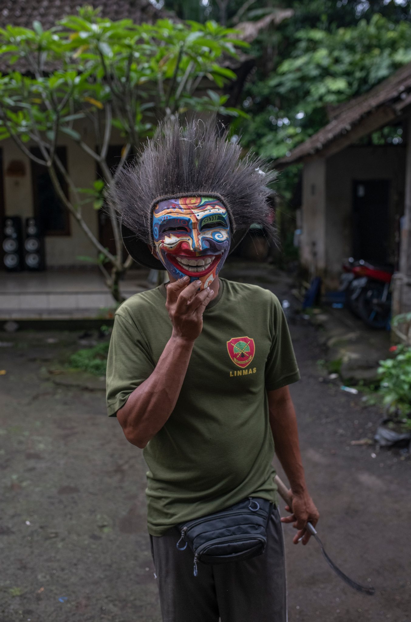 A man lifts a painted mask with a wild spray of hair to his face.