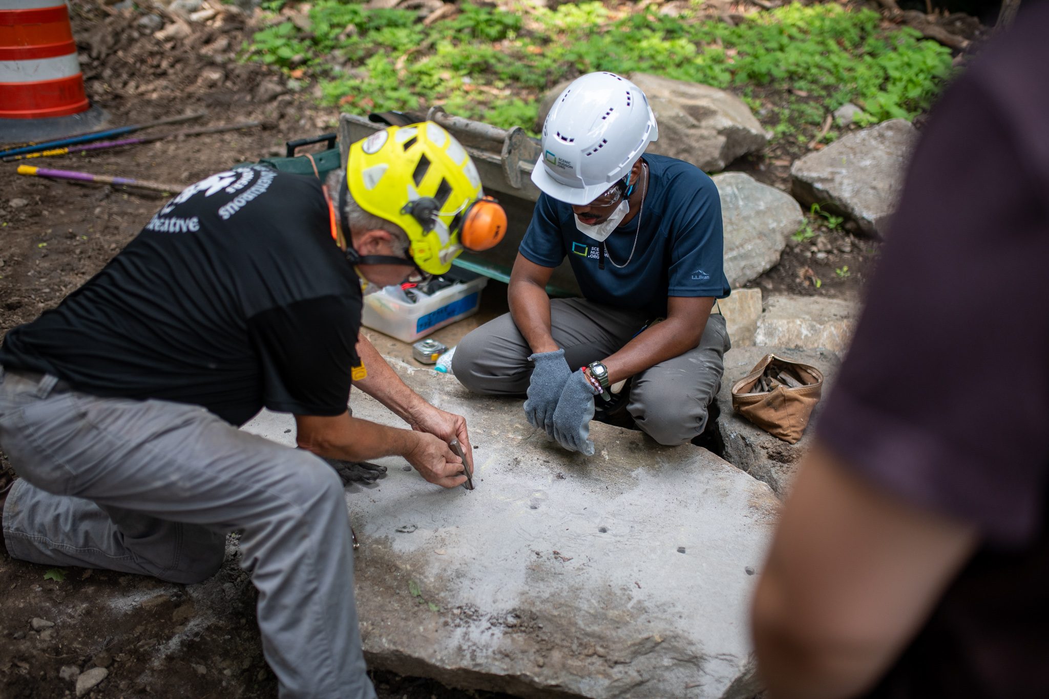 Two crew members kneel to mark and measure a new stone.