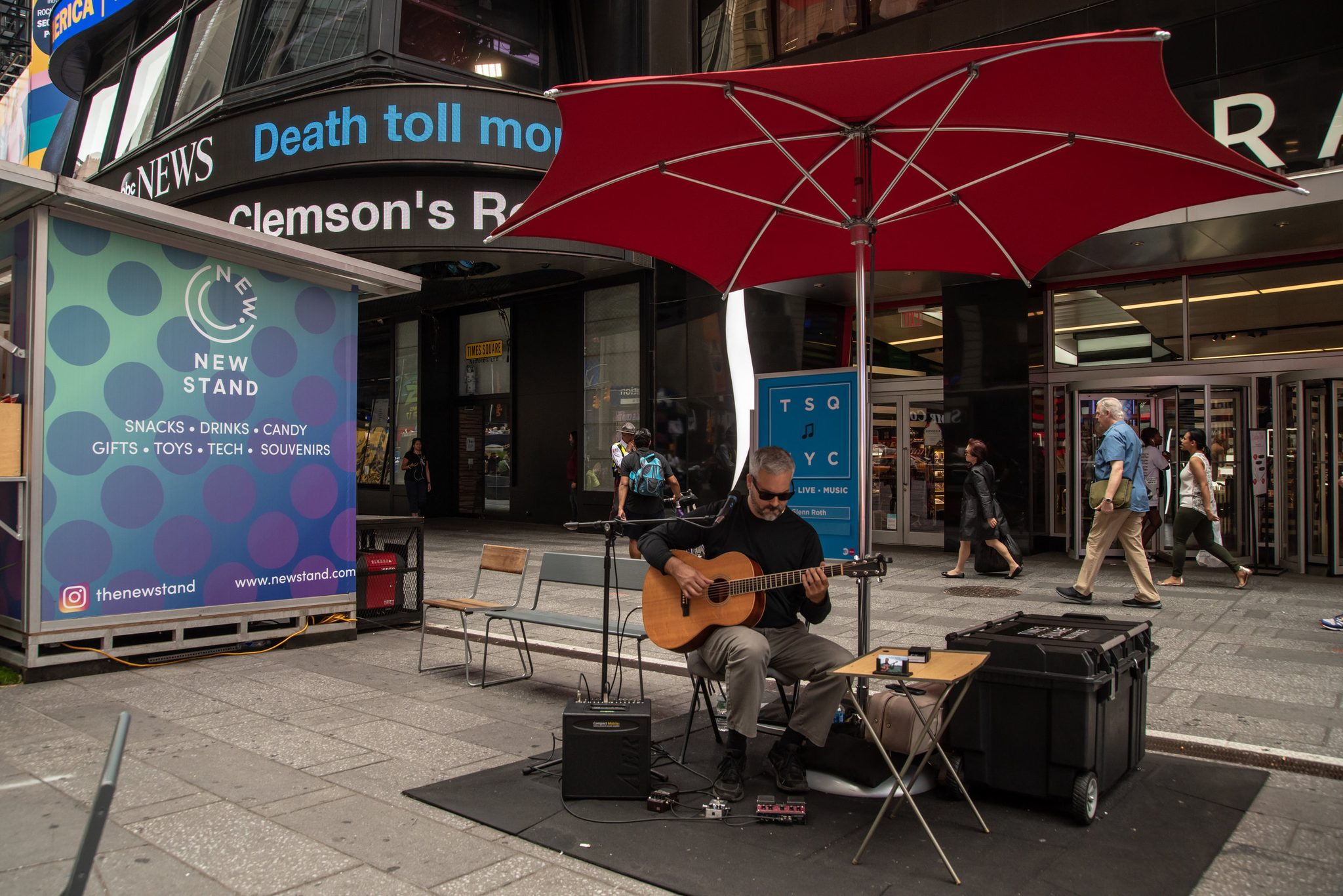 Under a red umbrella in Times Square, Glenn plays while the news ticker scrolls overhead.