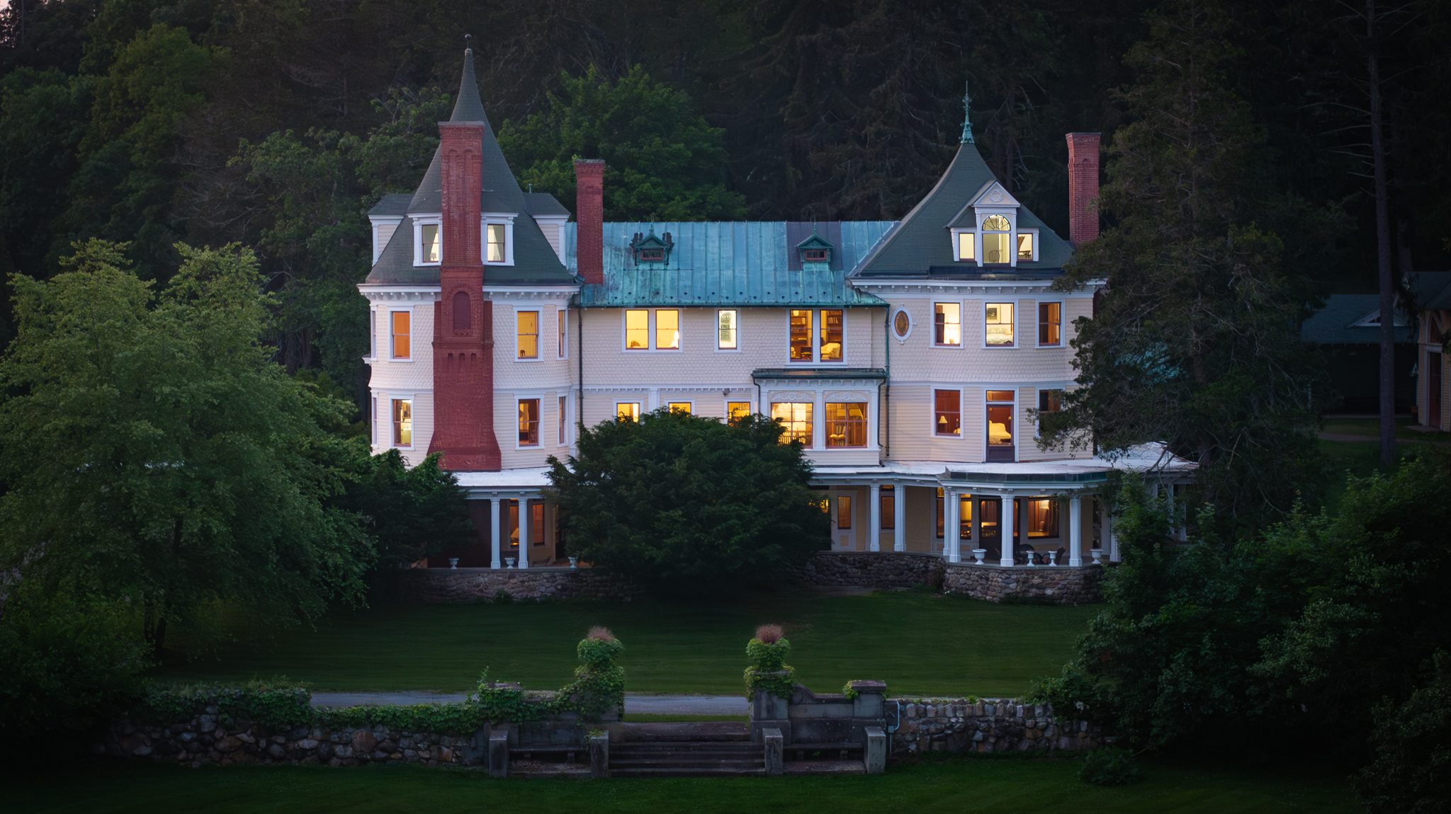 A tighter look as night comes on, lit rooms behind the shingle walls and the copper roof gone green-blue.