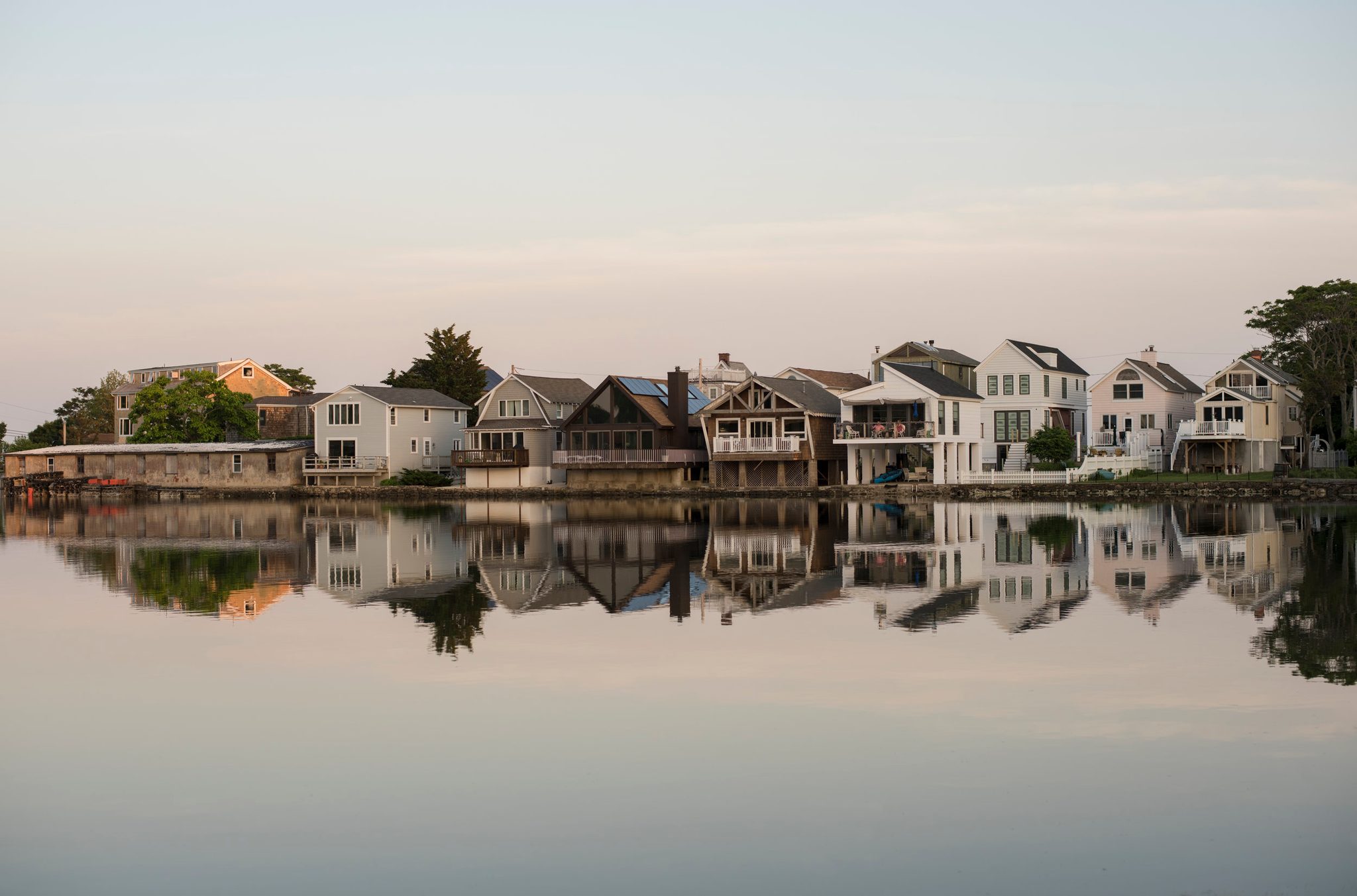 A row of shoreline houses doubles itself in the glassy water at dusk.
