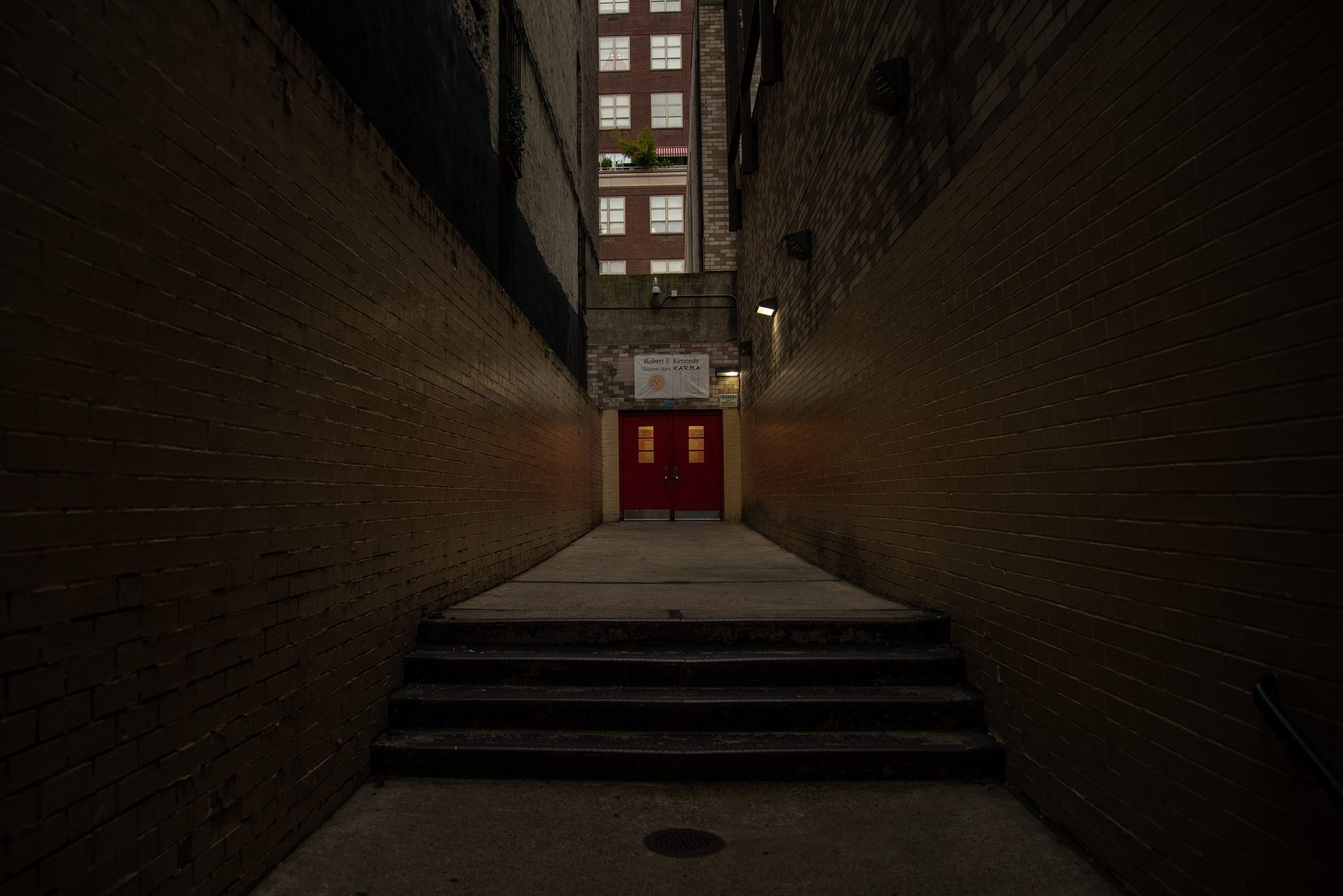 A narrow brick passage ends at a red door.