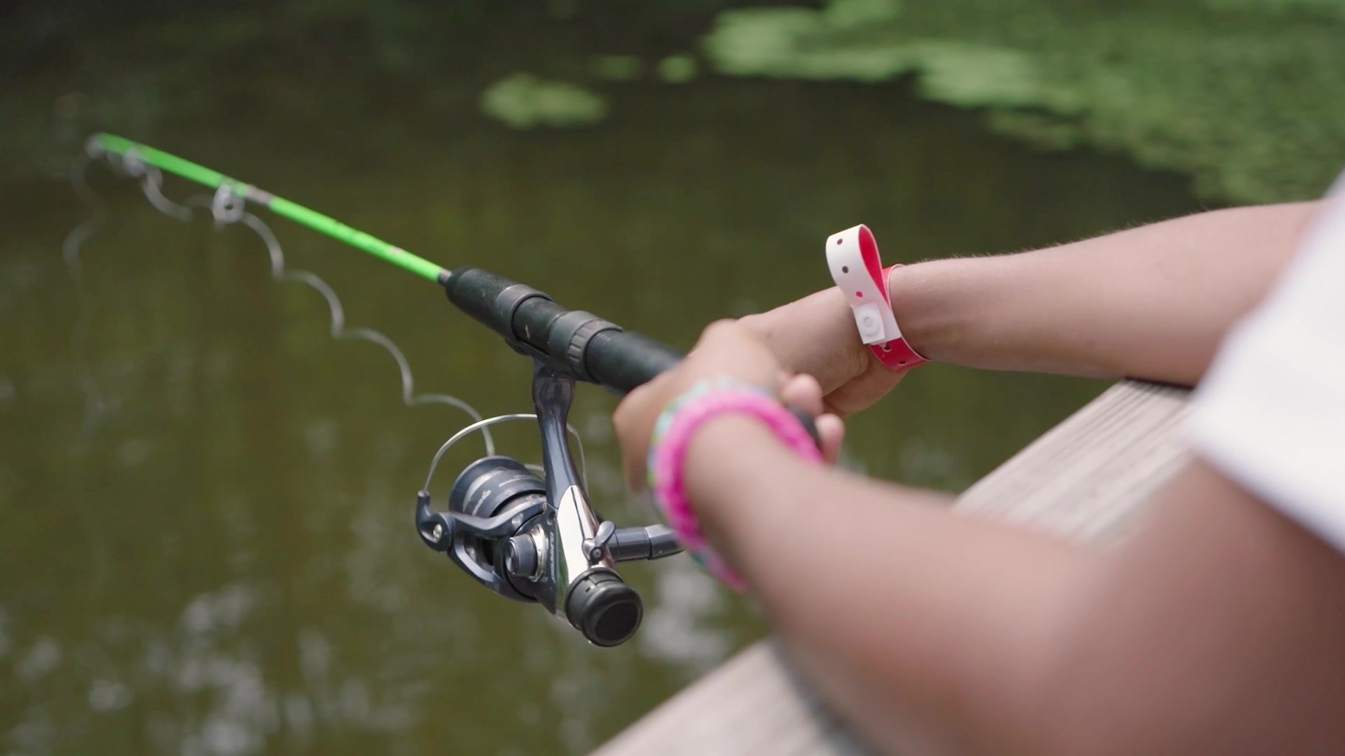 A line in the water off the dock, bracelets on the wrist that holds the rod.