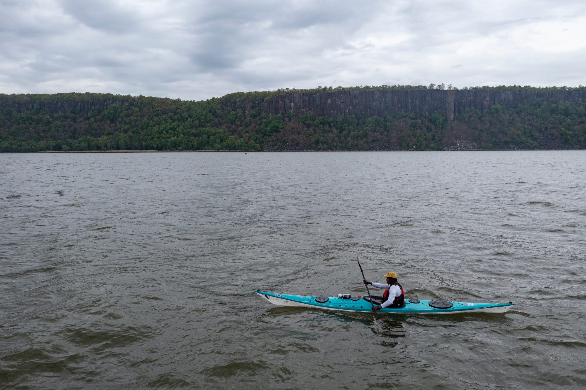One kayak alone on a wide stretch of river, the wooded cliffs of the far shore running flat to the horizon.