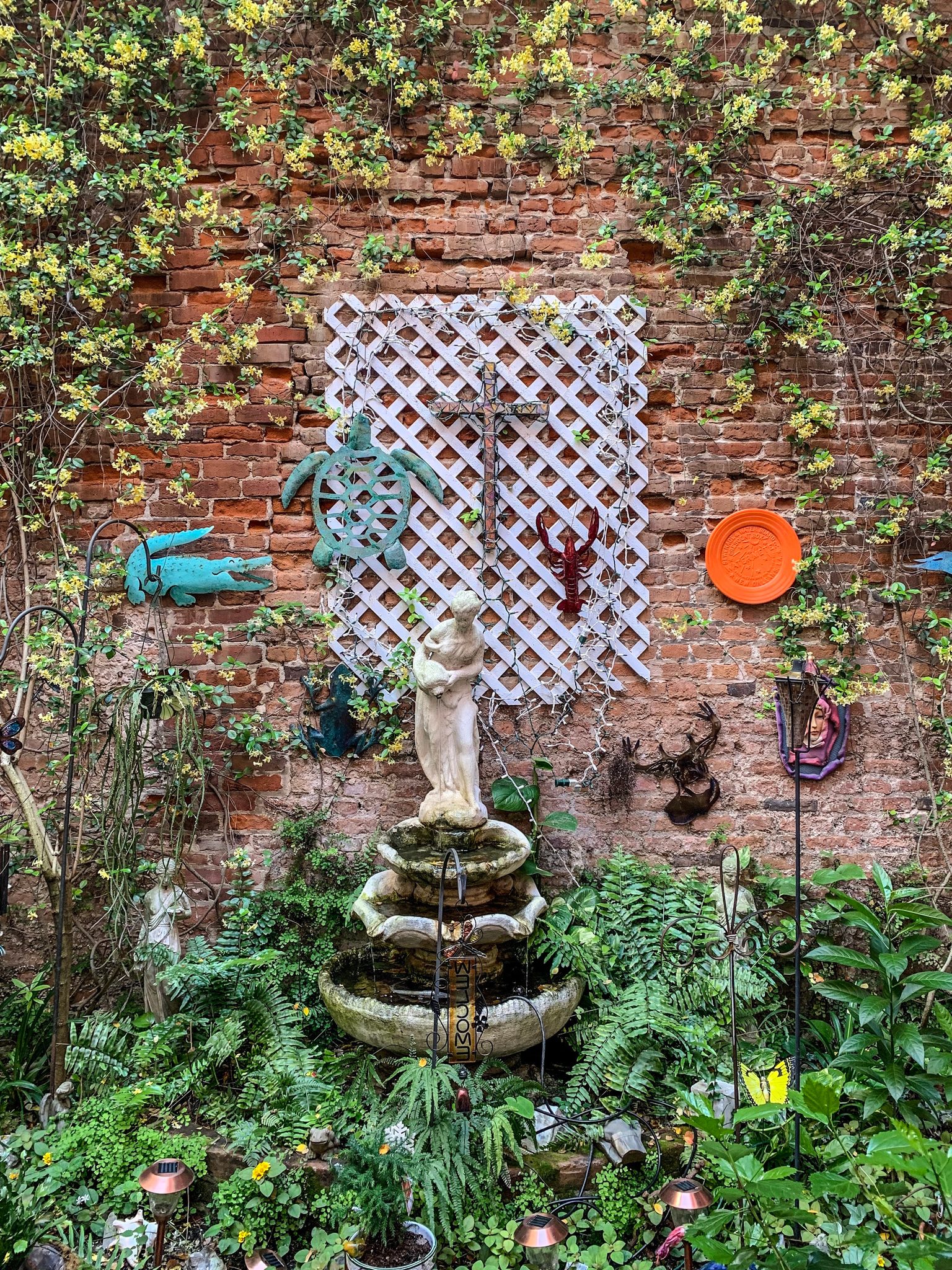 A tiny fountain garden climbs a brick wall hung with lattice and found things.