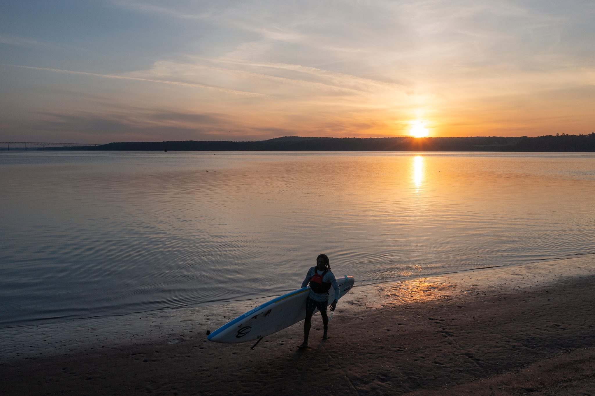 A silhouette walks the board down to the waterline, the sun a hot dot on the horizon.