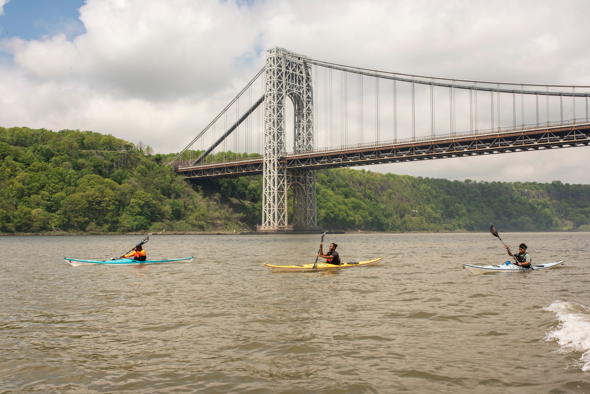 Three boats line up across the river, the bridge tower rising out of the trees on the Jersey side.