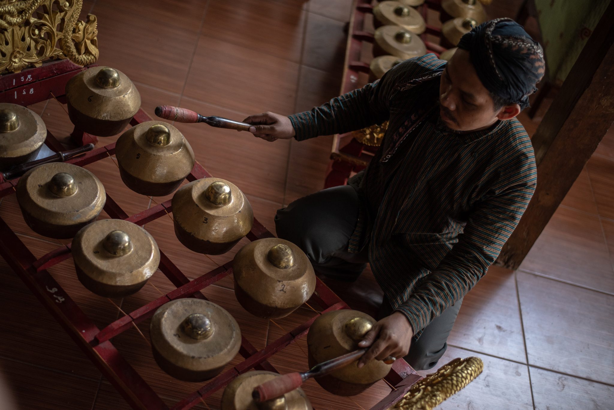 He sits down at the bonang and lets the kettle gongs answer his mallets.