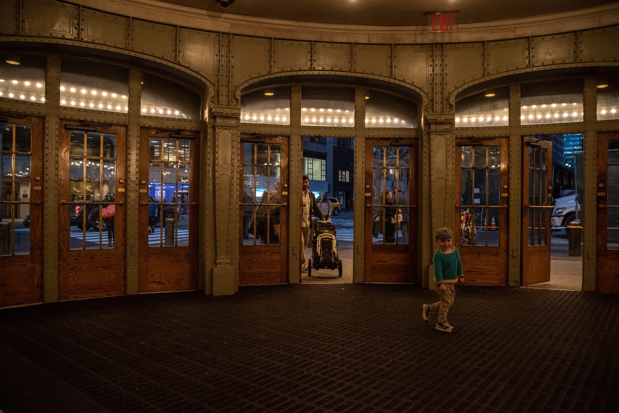 Ronin toddles across the empty vestibule toward the doors, the stroller waiting behind.