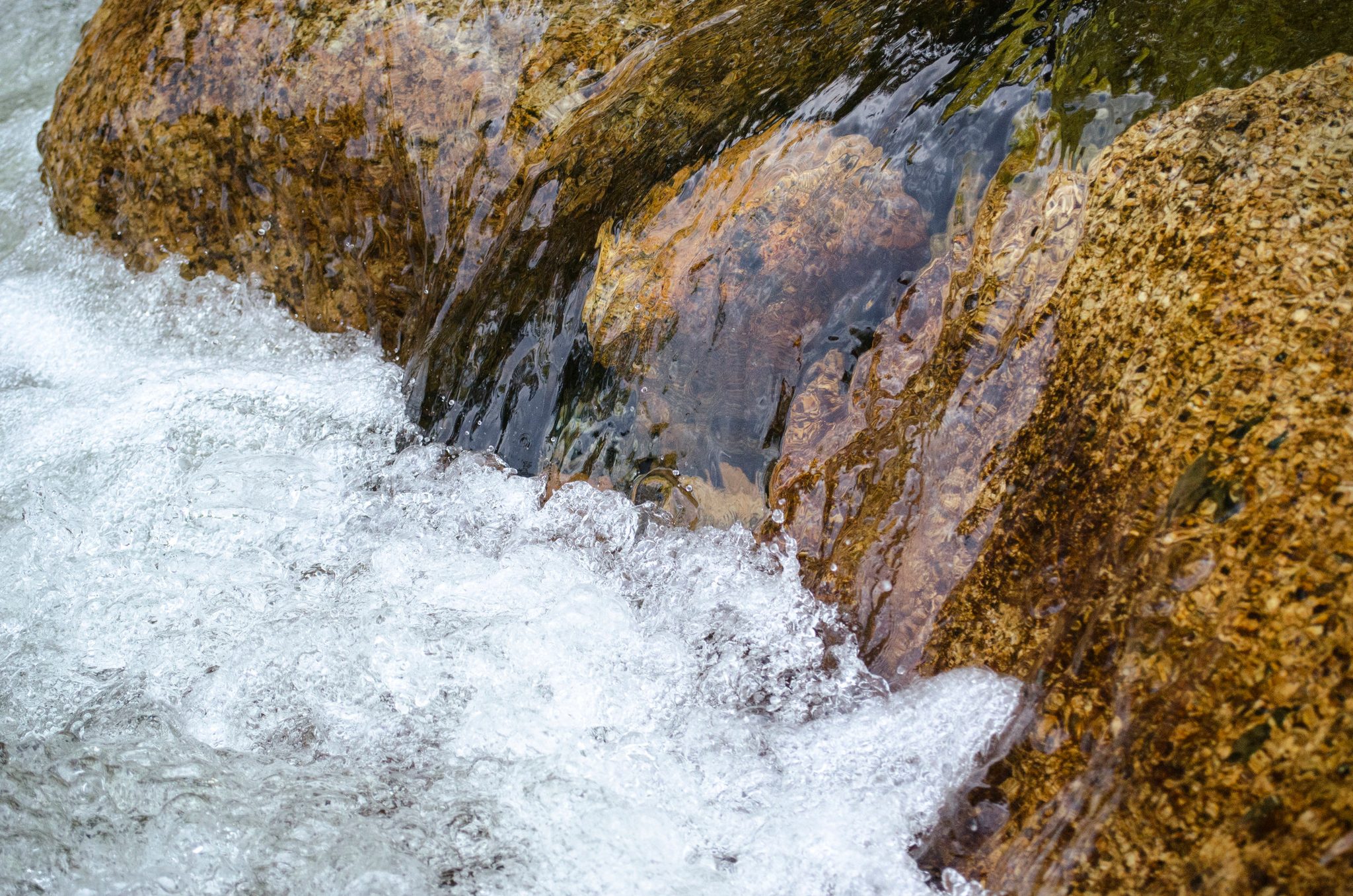 Clear water rushes over golden rock.