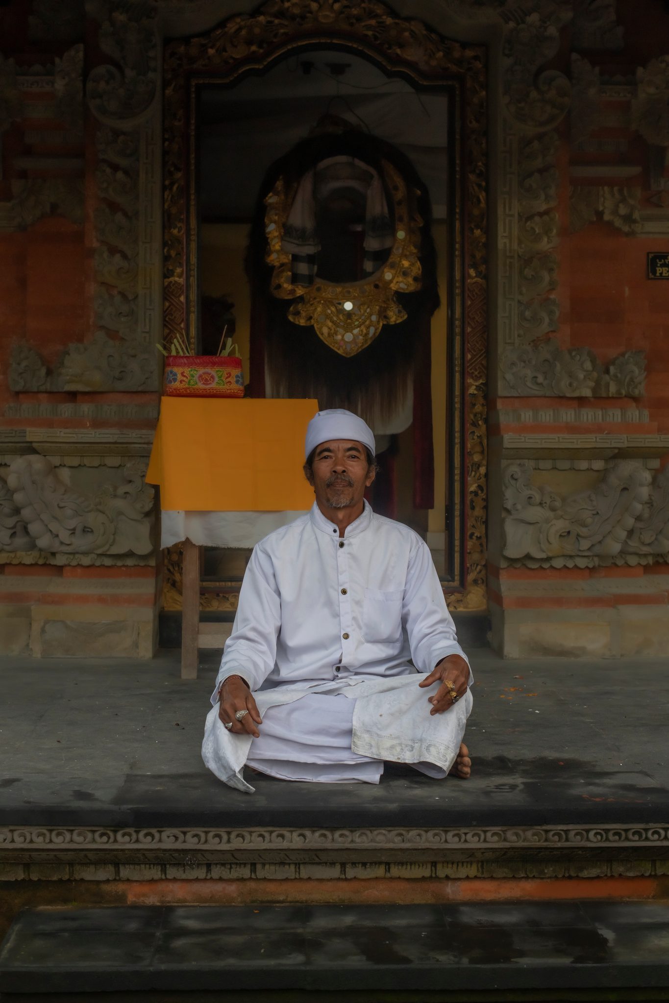 Dressed in white, he sits cross-legged in the doorway of the shrine.