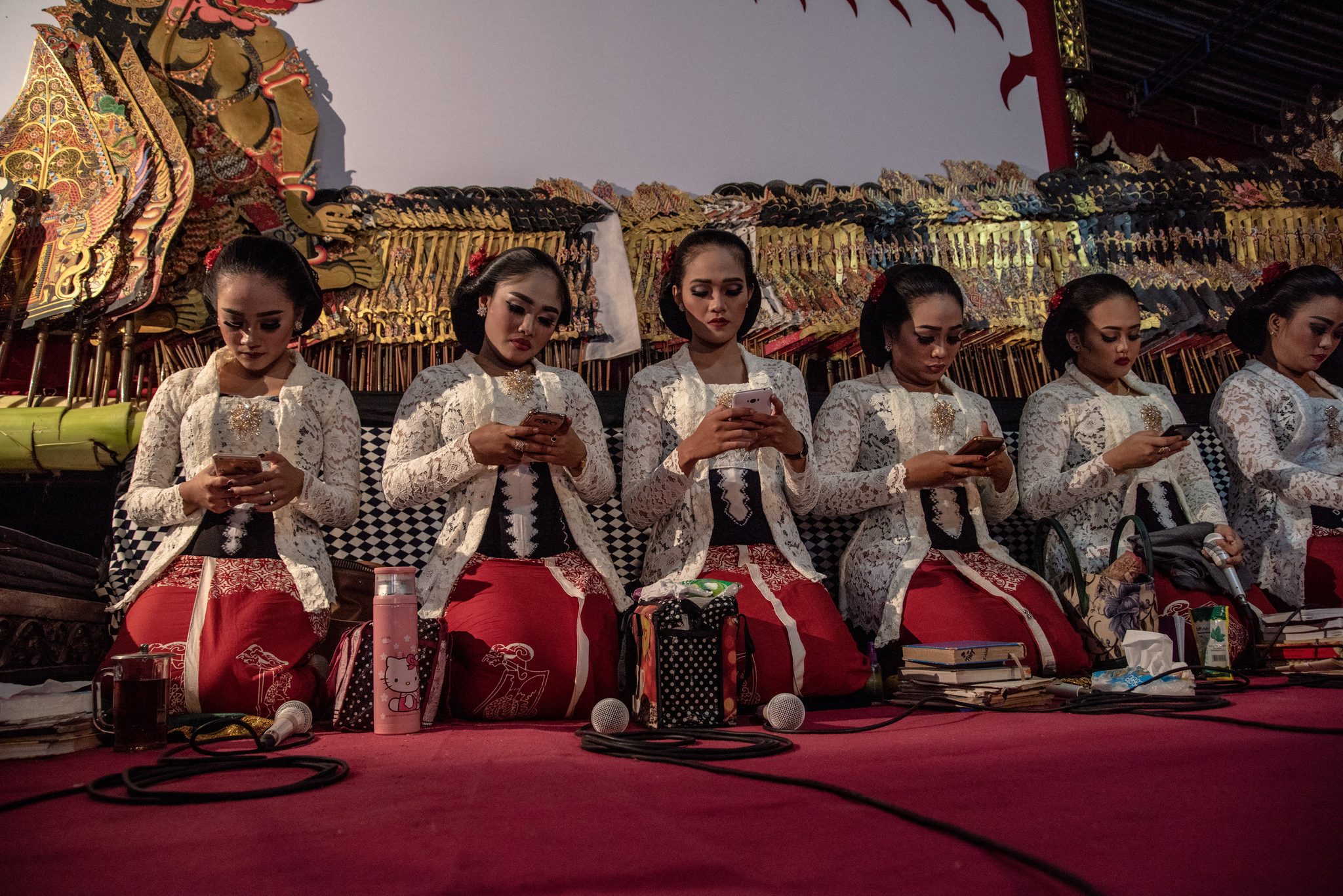 Six singers wait their turn, every one of them on her phone.