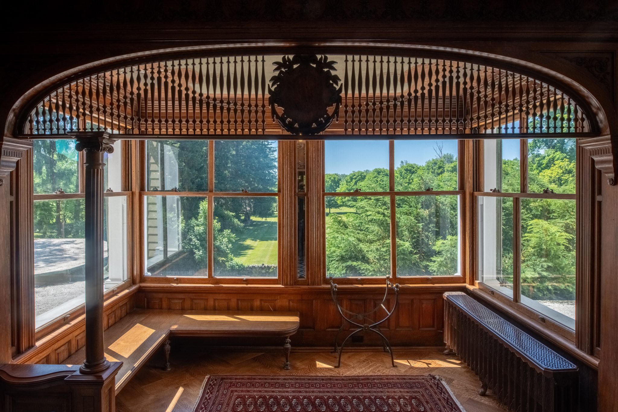 A window seat under a carved spindle arch, afternoon sun falling across the oak bench and parquet floor.