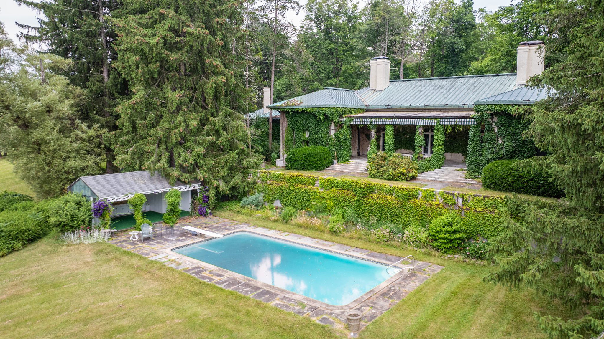 The bungalow from above, a long ivy-covered house with a green metal roof, terraced gardens and a stone-edged pool.
