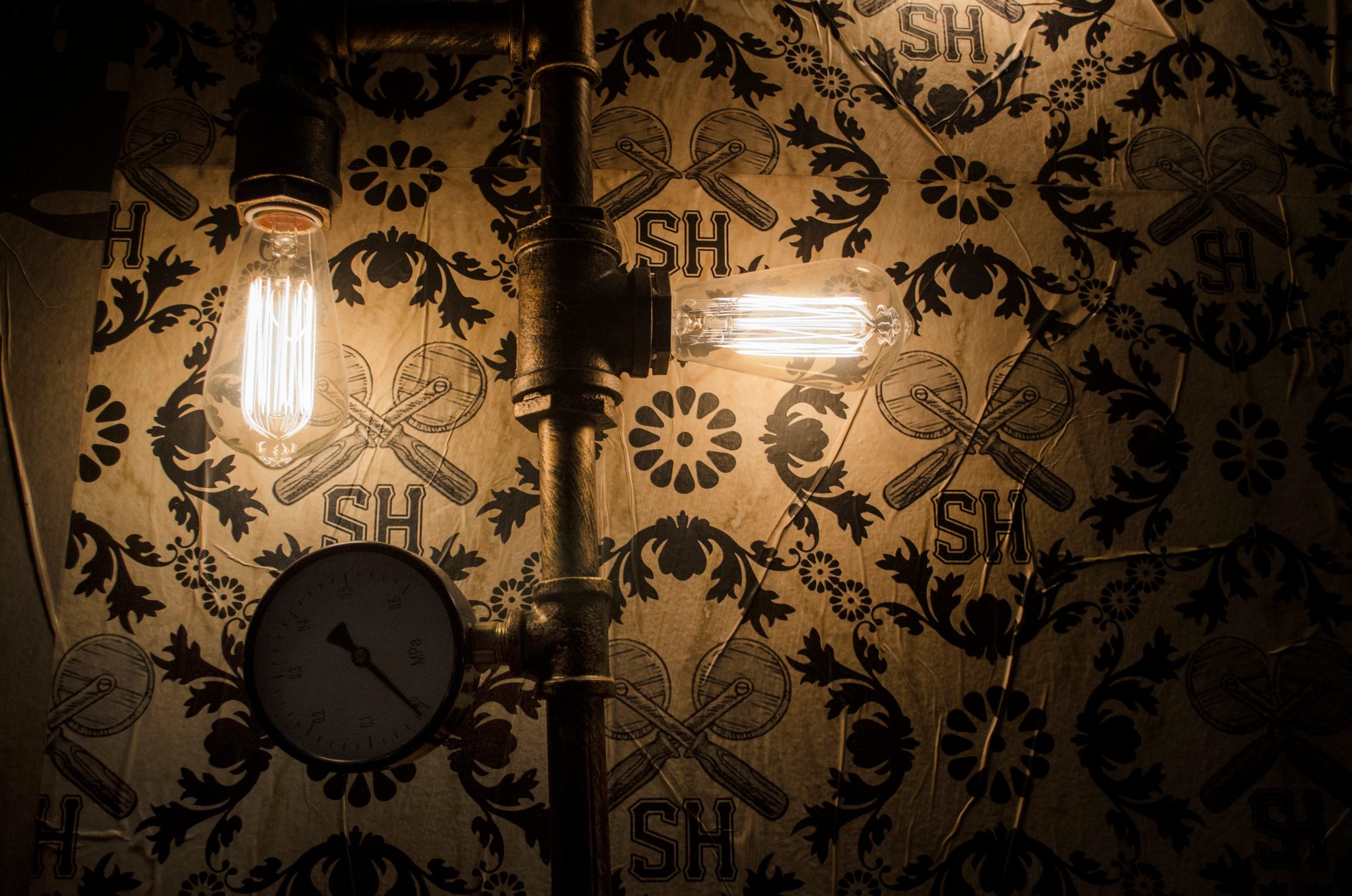 Edison bulbs glow against patterned wallpaper, a pressure gauge below.