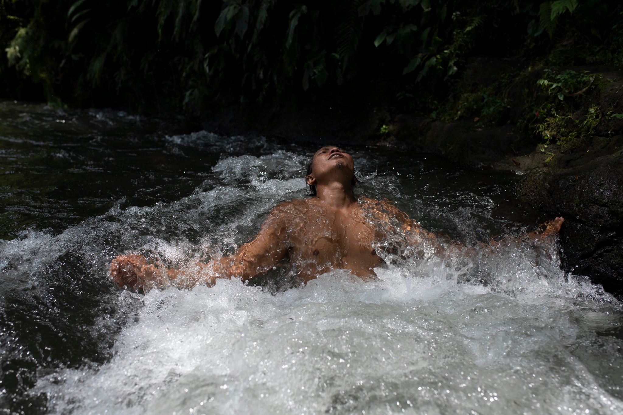 White water breaks over his chest as he floats with his eyes closed.