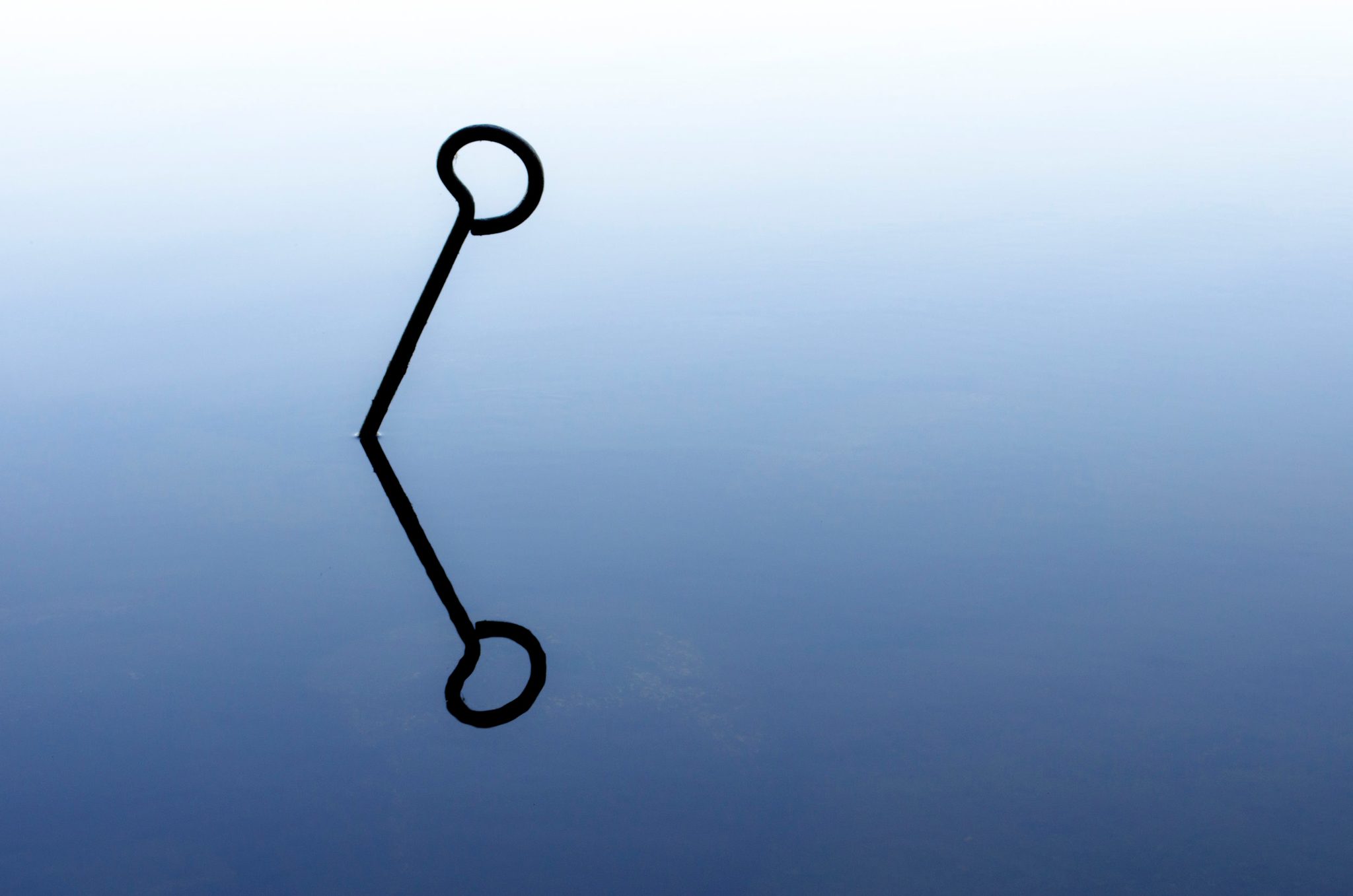 A mooring ring and its reflection on a sheet of blue water.