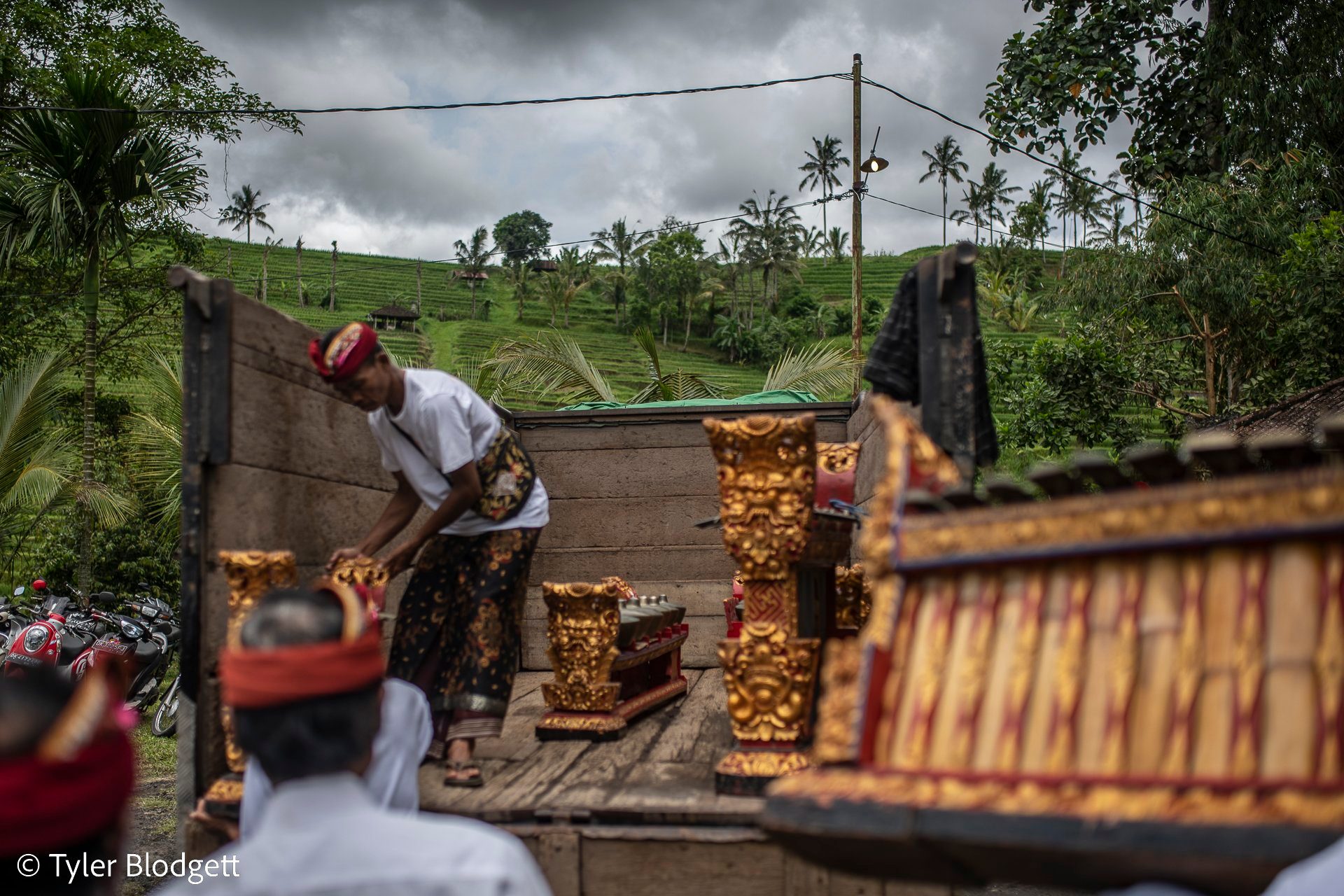 Gilded gamelan frames come off the back of a truck, rice terraces rising behind them.