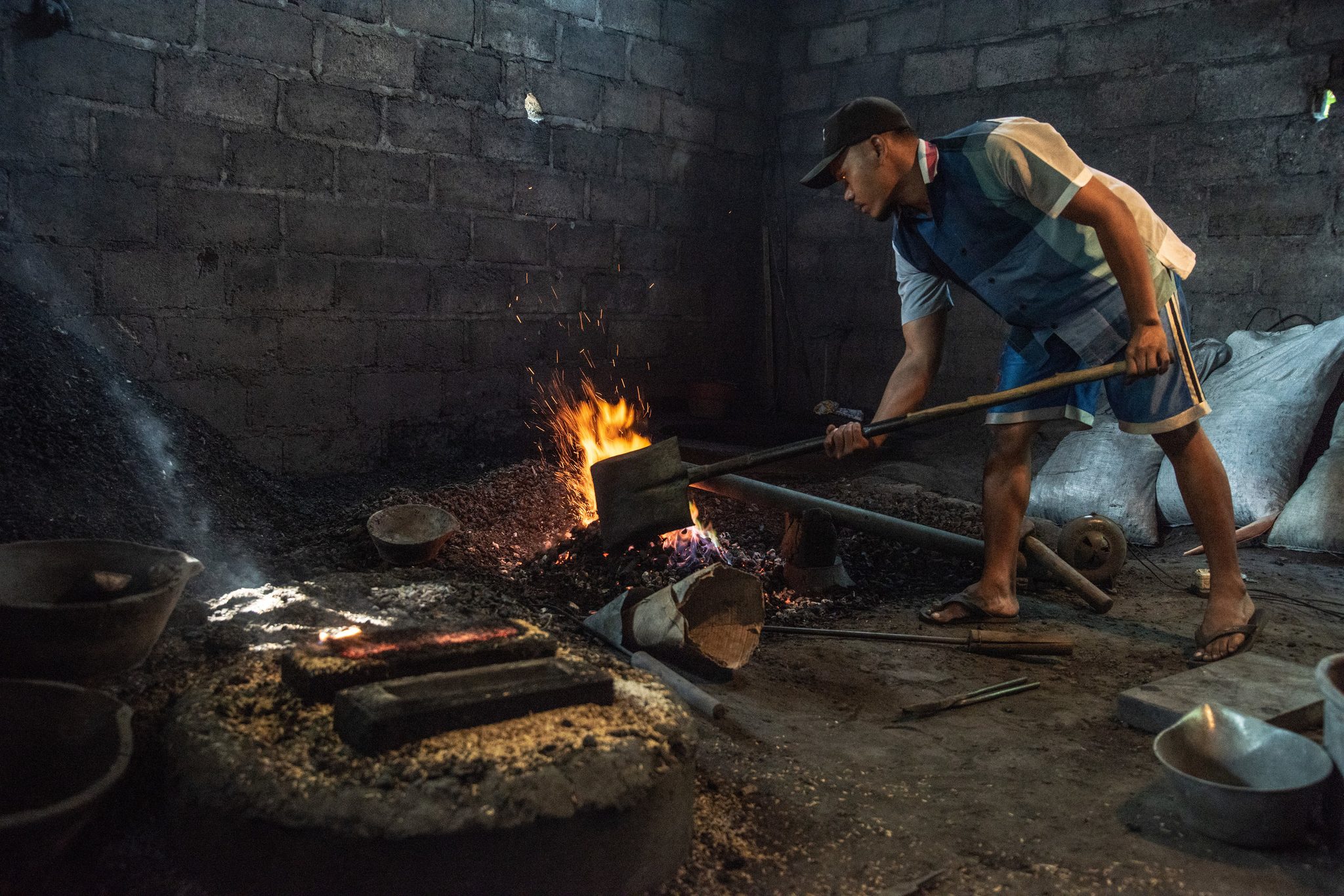 A worker draws a glowing bar from the coals with long tongs.