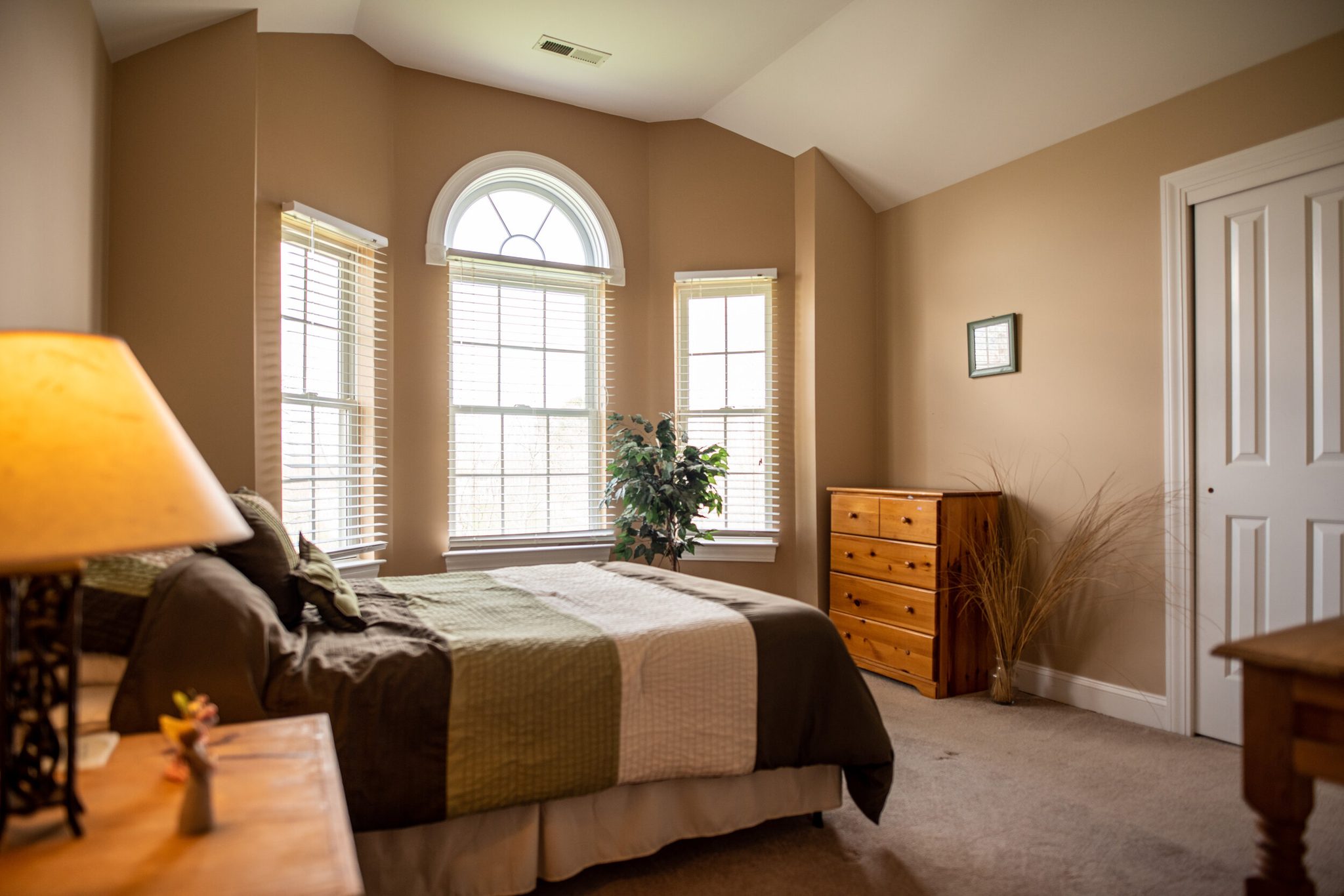 A quiet bedroom under an arched window, a lamp left on by the bed.