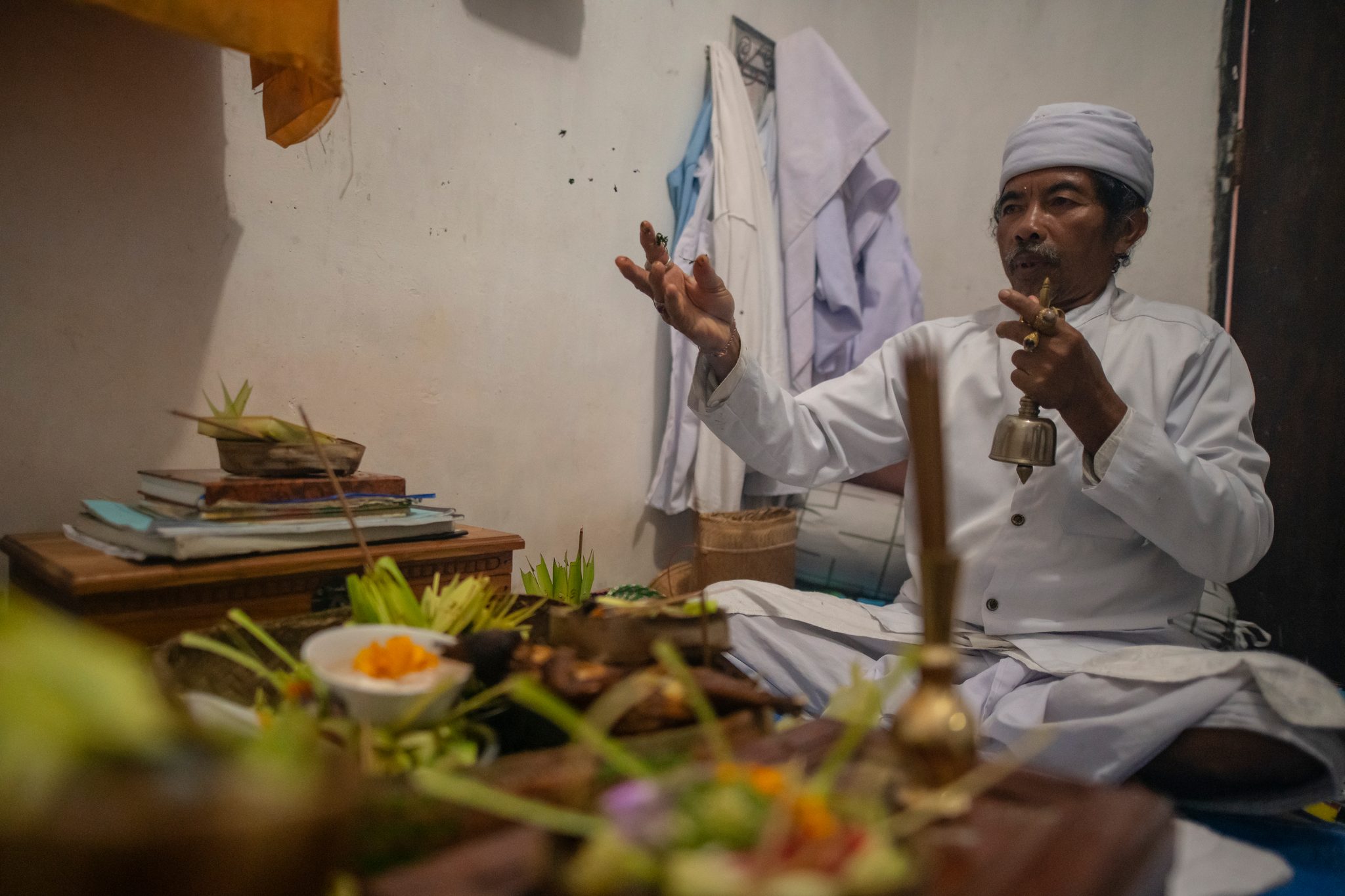 A priest in white rings his bell over the offerings.