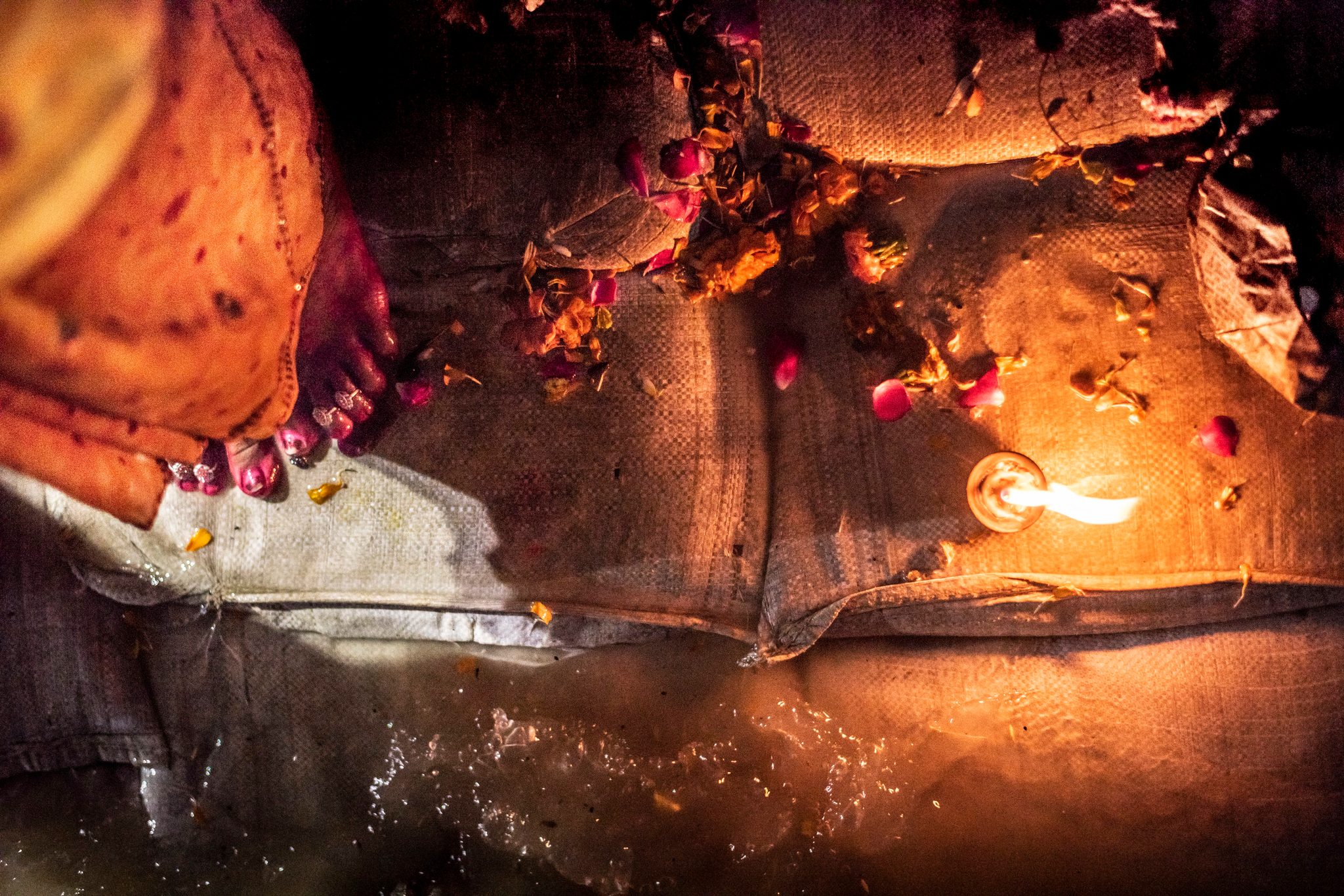 Woman stands amidst flower petals on the edge of the Ganges.