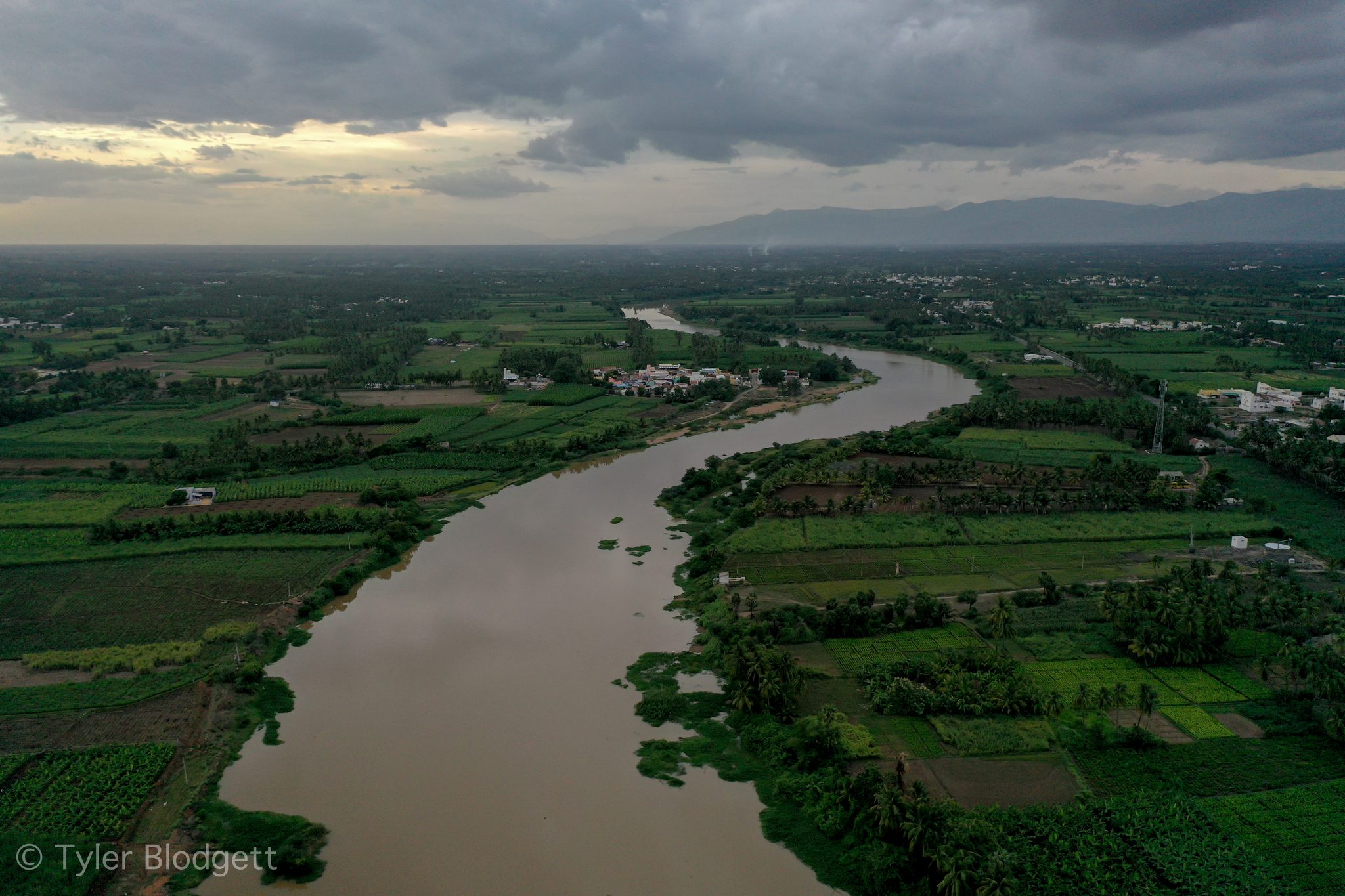 The river bends through green farmland beneath a stormy sky.
