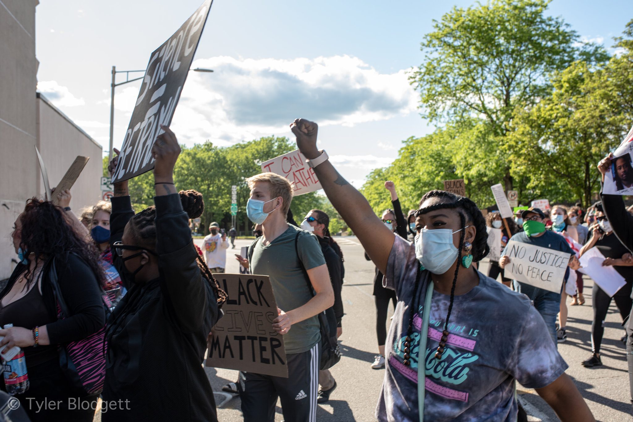 Fists go up as the march turns the corner, a sign reading No Justice No Peace held just behind.