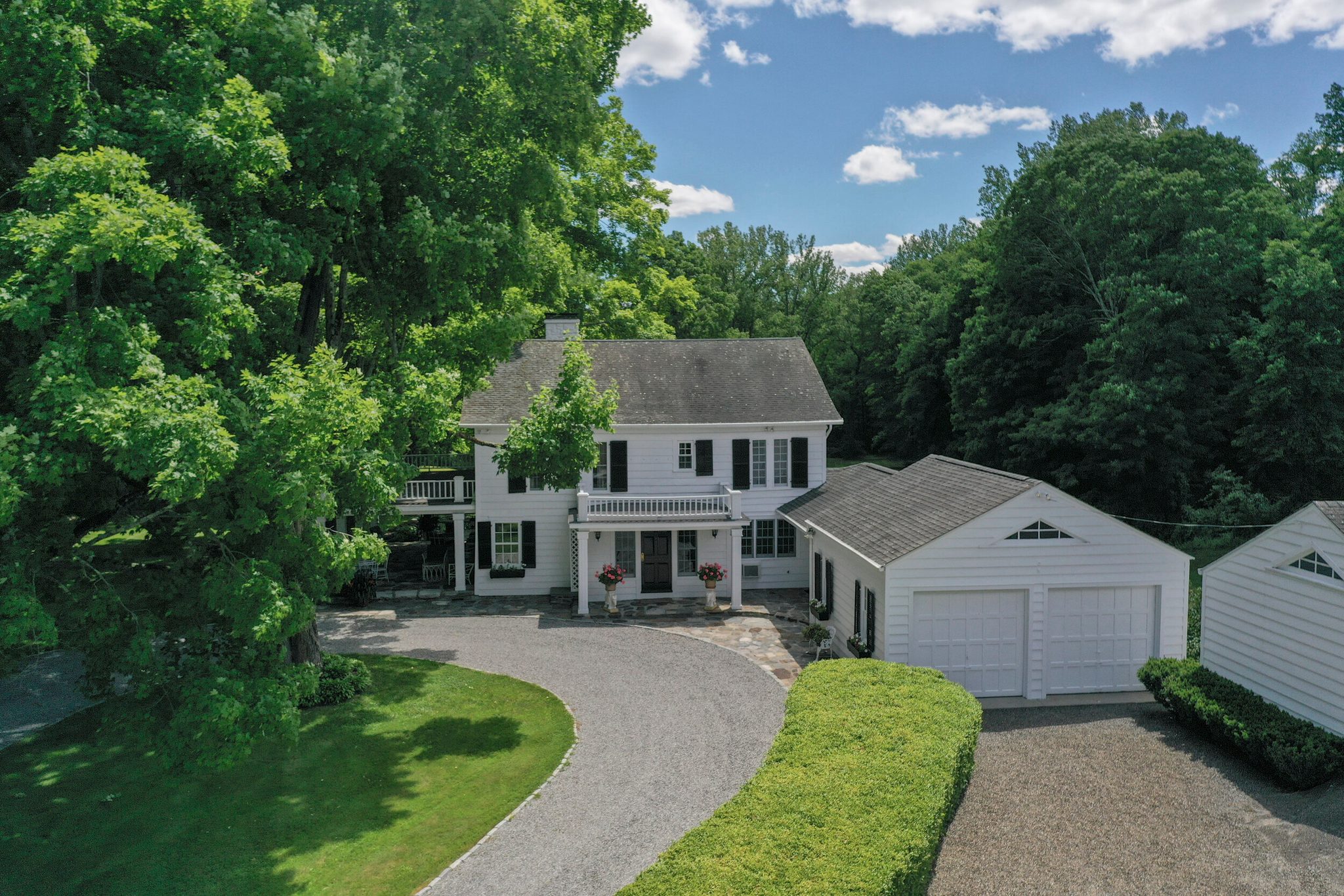 A white colonial and its carriage house sit at the end of a curving gravel drive.