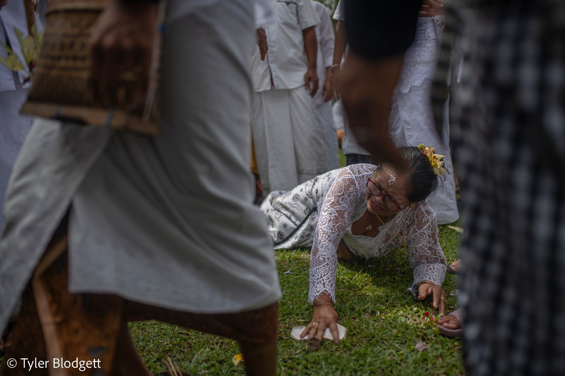 A woman sinks to the grass in the middle of the ceremony, hands pressed to the earth, as the crowd moves around her.