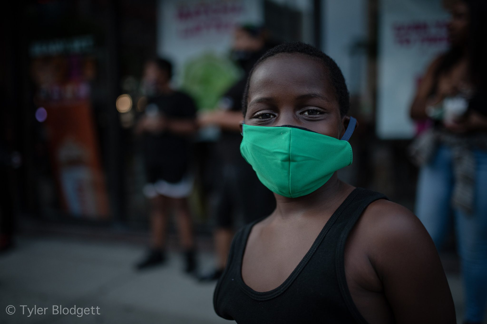 On Juneteenth, a woman in a green mask stands in the evening street as the march gathers.