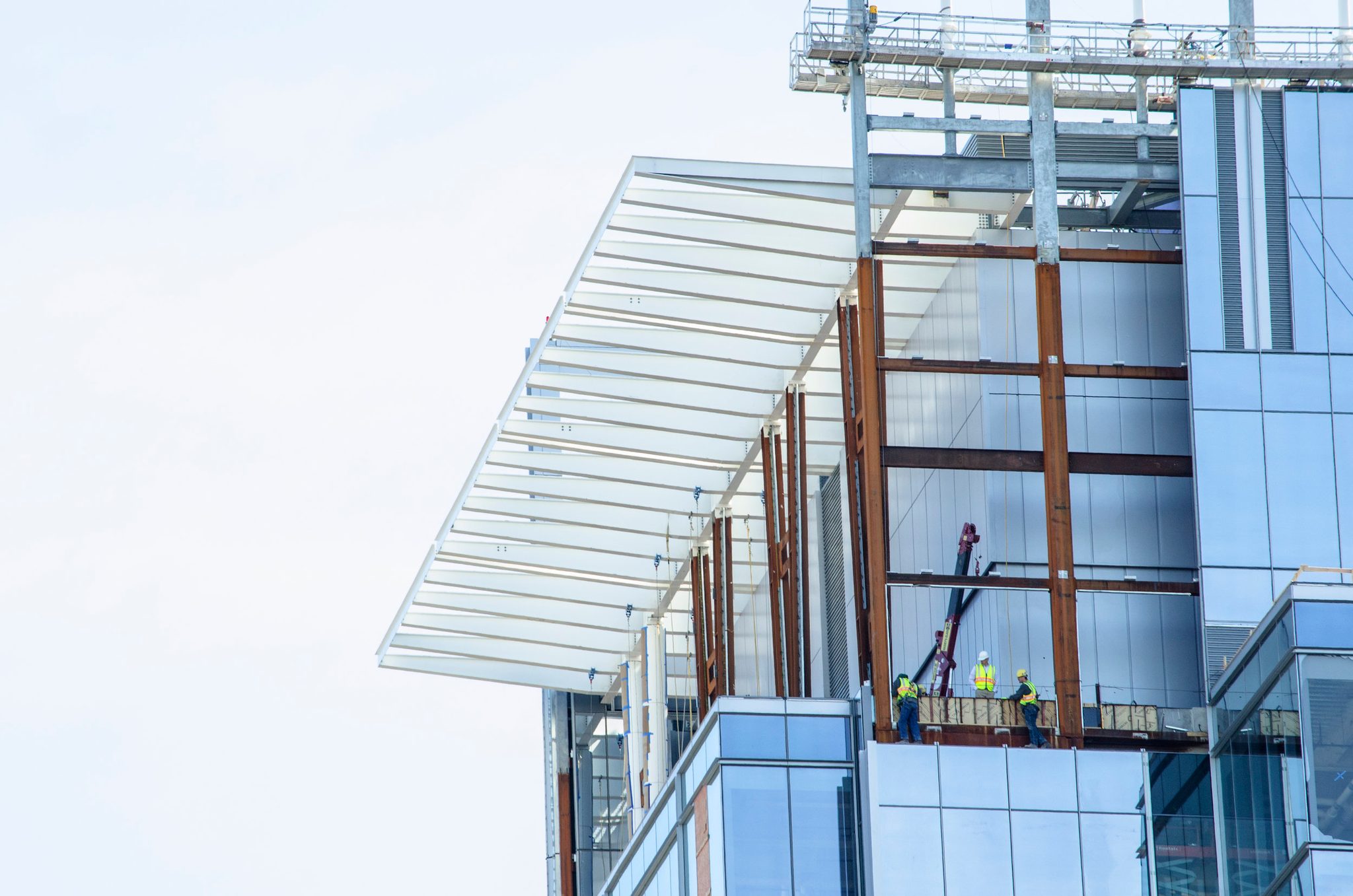 Workers in hard hats stand high on the glass tower as it rises.