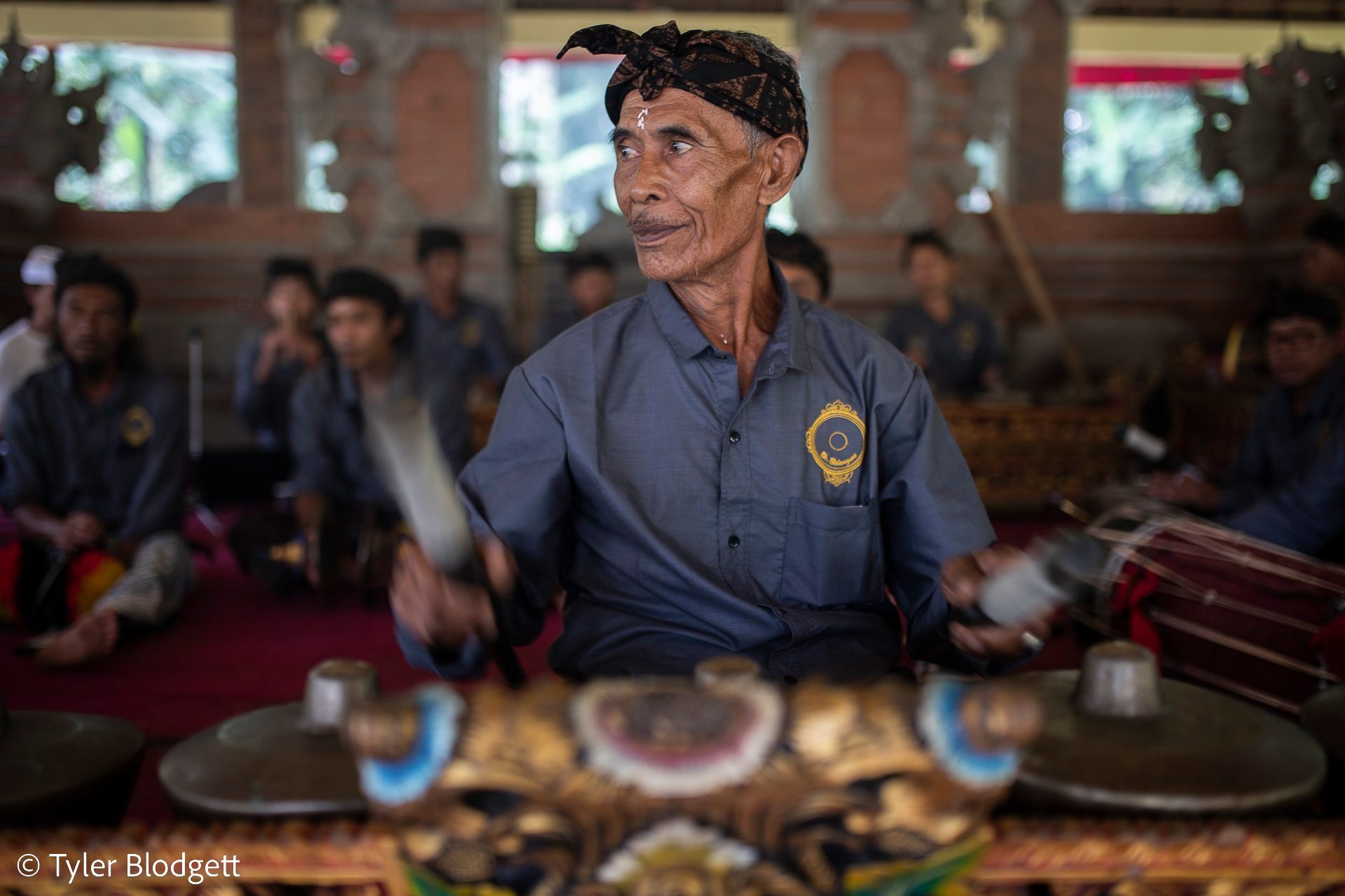 An elder of the gamelan plays without looking down, his eyes on something across the pavilion.