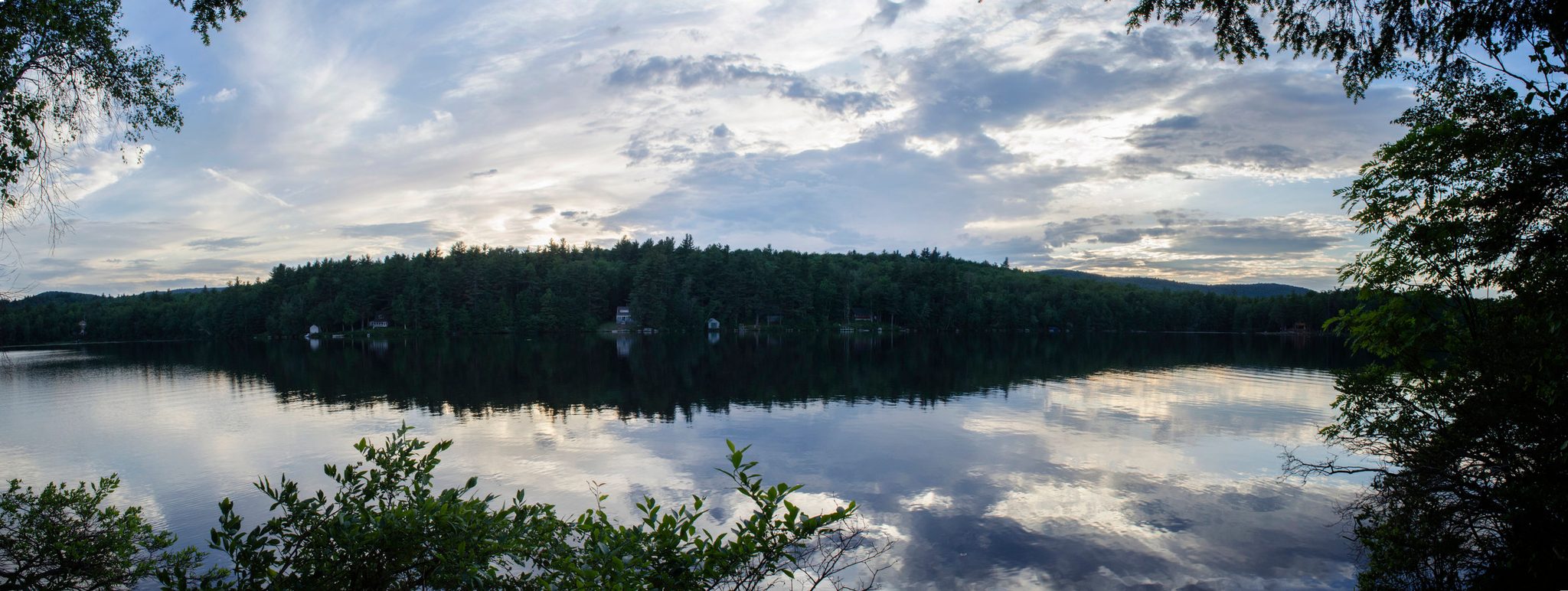 A lake mirrors the forest and the summer clouds.