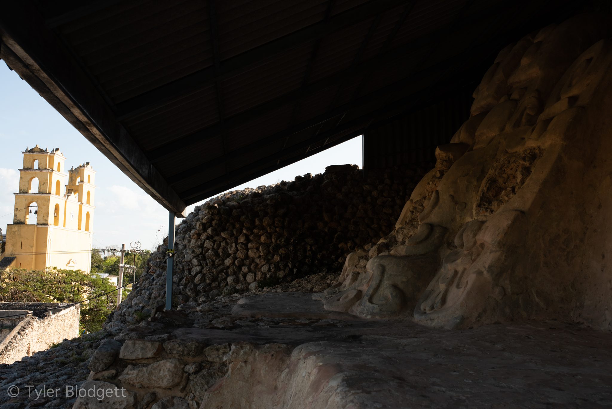 A yellow church bell tower rises beyond a heap of old stones.