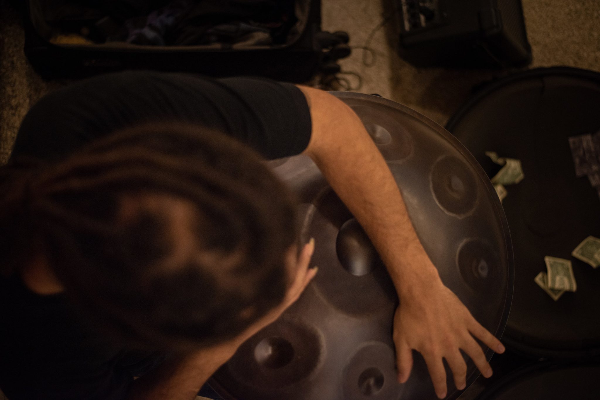 From above, his hands move across the steel of the Hang, a few bills tucked at its rim.