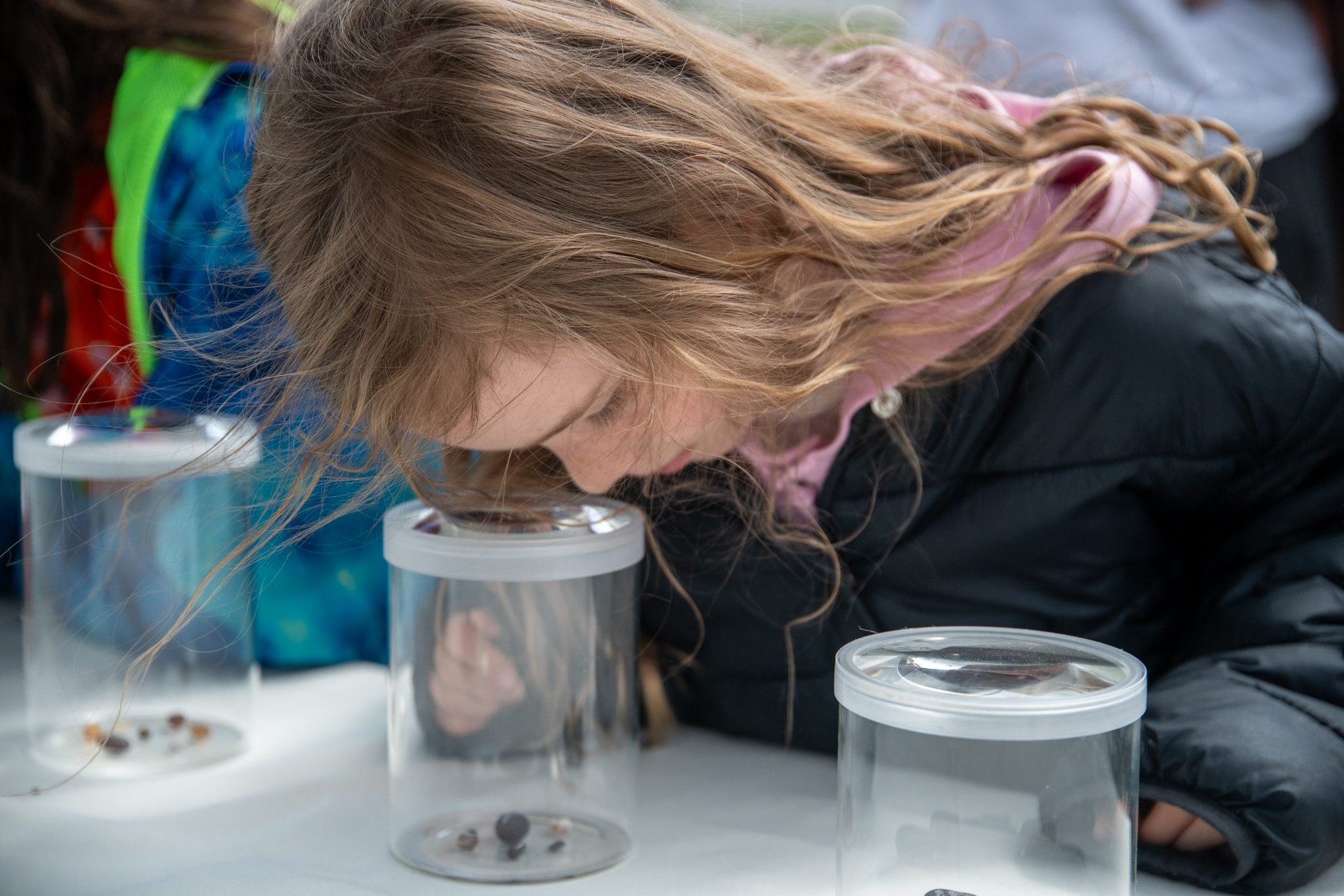 A girl buries her nose in a jar to see what's inside.