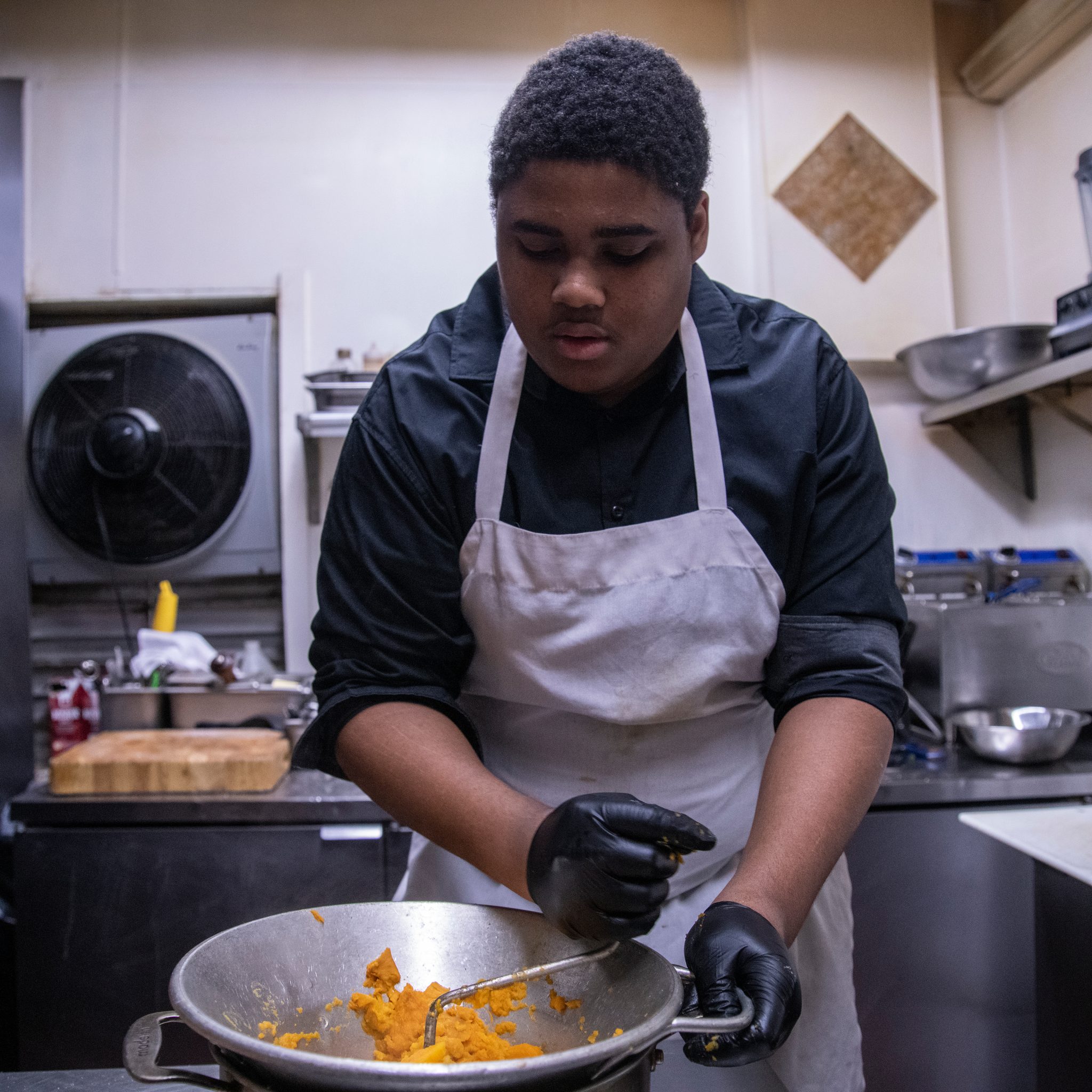 Apron on, a young cook stirs a pan of vegetables.