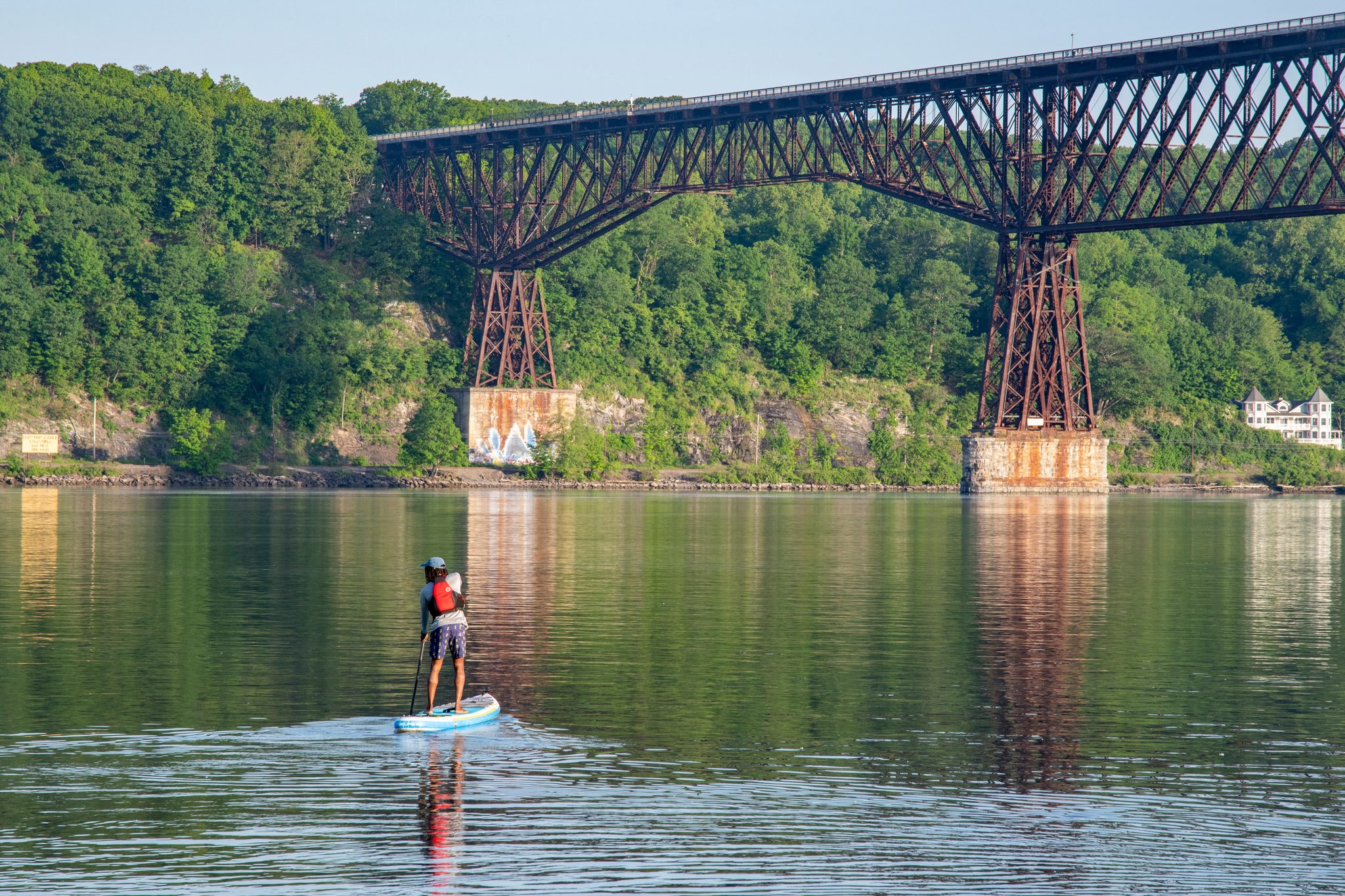 Chev paddles under the dark iron trestle, the bridge doubled in the still water.